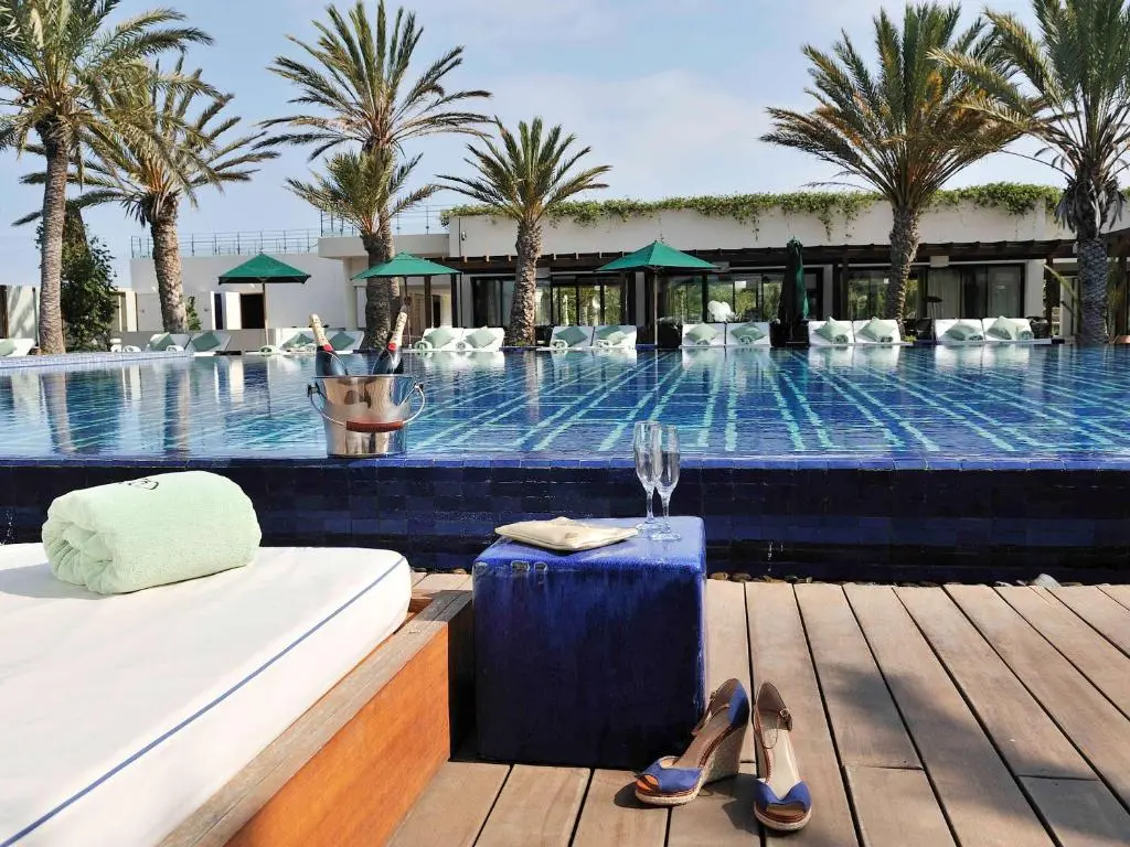 A sunbed with a complimentary towel with two whine bottles on the pools edge