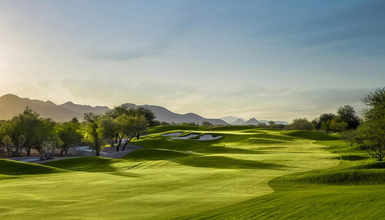 Golden sunset light casts long shadows across a pristine golf fairway.
