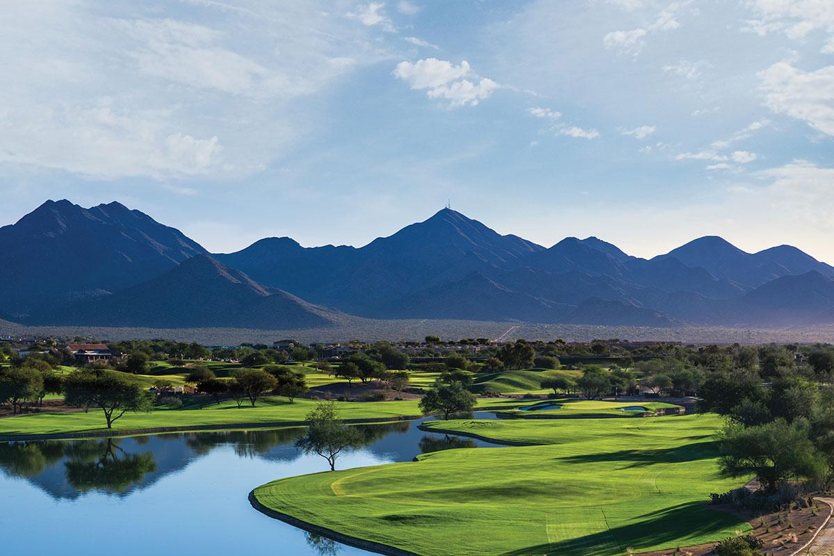A golf course with a lake reflecting the surrounding mountains and trees.