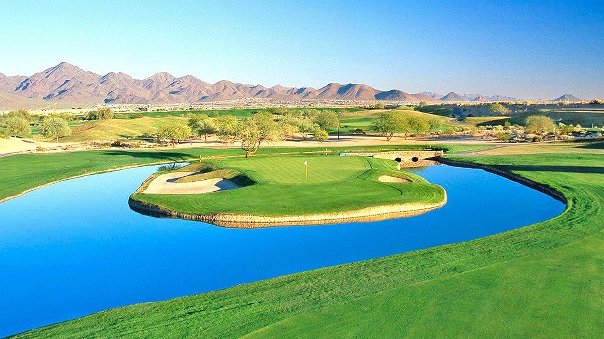 A stunning island green surrounded by bright blue water with desert mountains in the background.