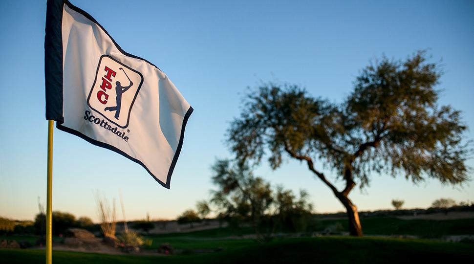 Close-up of a TPC Scottsdale flag waving with a lone tree in the background.
