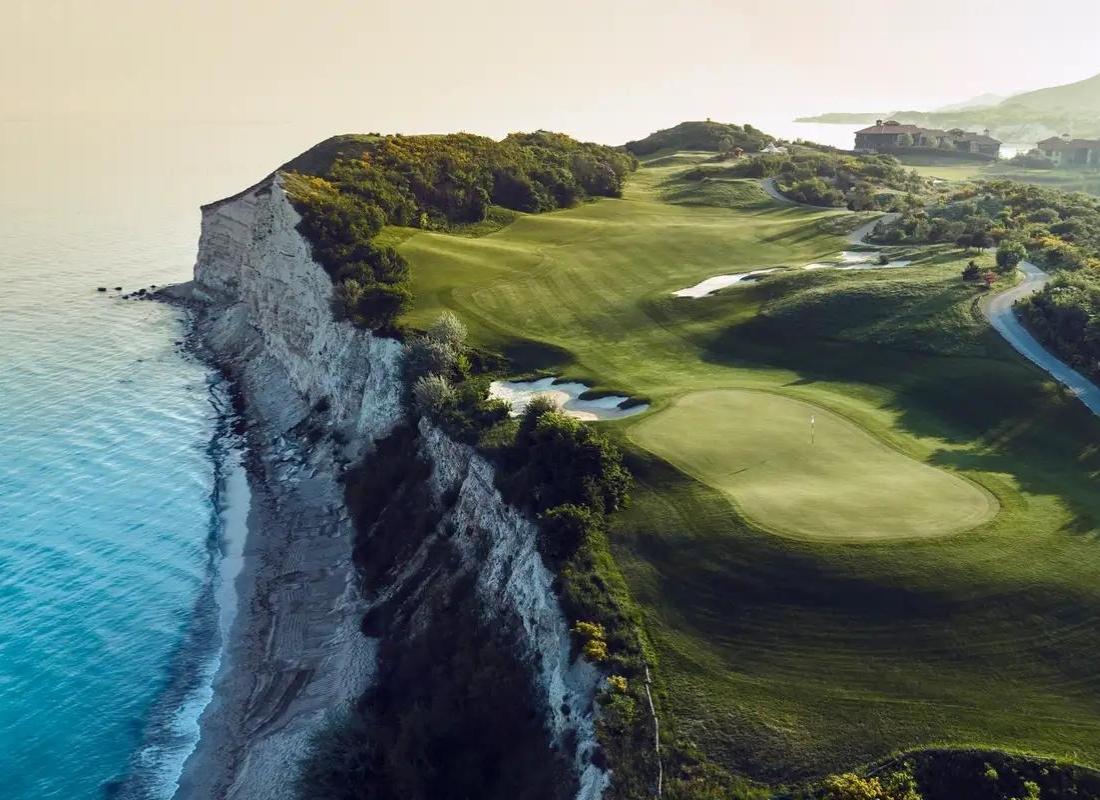 Overhead view of a well maintained green on the cliff side with a large strategically placed sand bunker