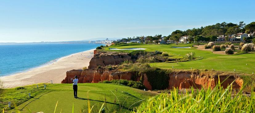 Player taking their tee shot on a long carry, cliffside Par 3 with the beach on the left