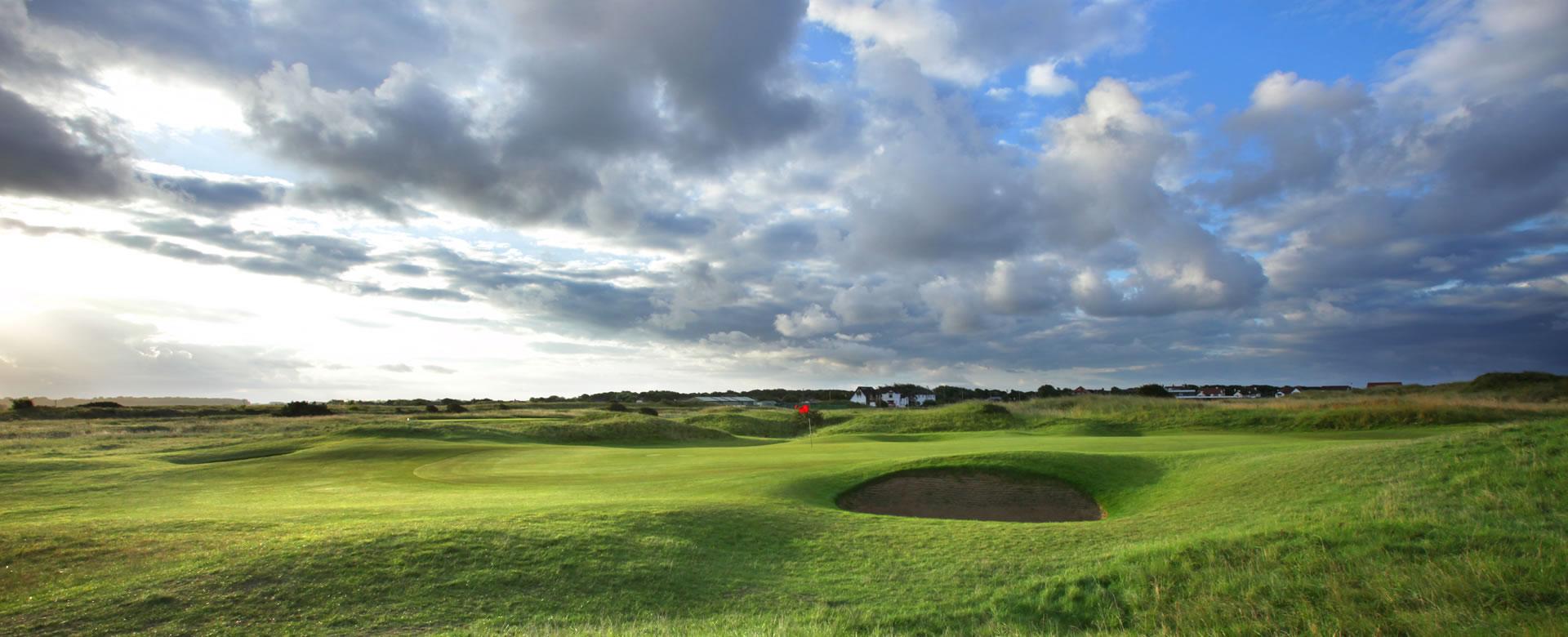 A green with a deep bunker under dramatic cloudy skies.