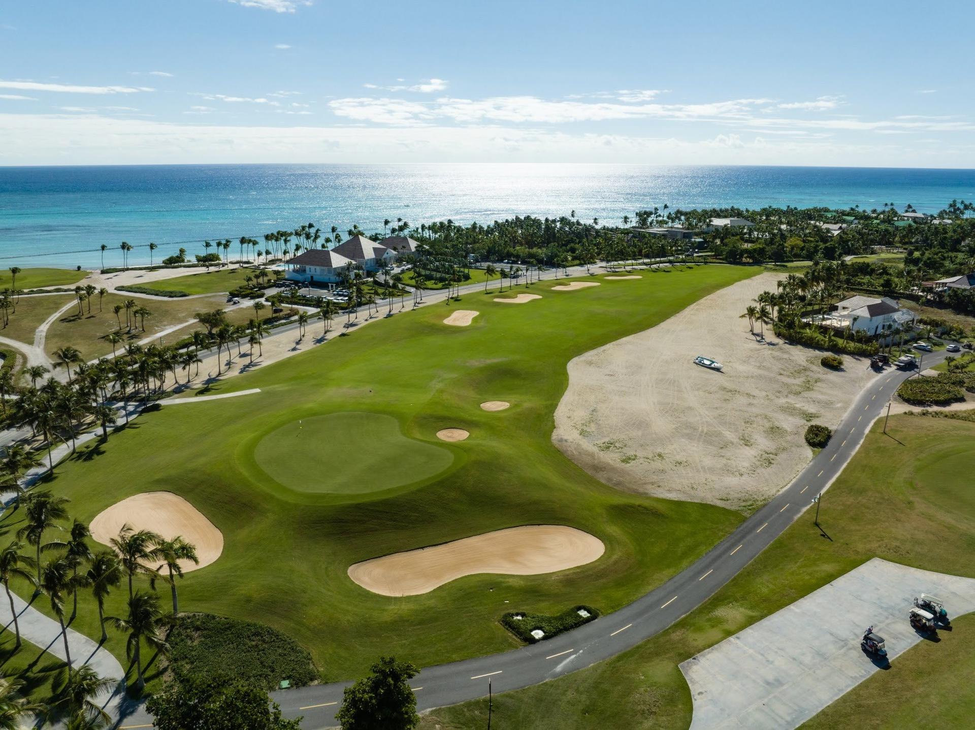 Overhead view of an elevated green surrounded by sand bunkers with coastal views in the distance