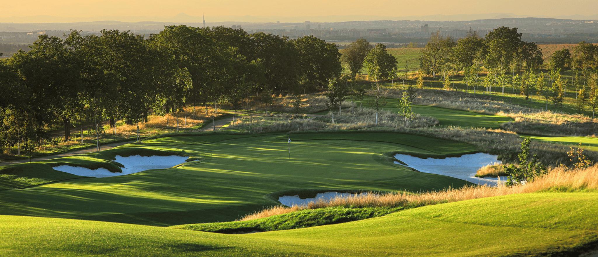 Panoramic view of a downhill fairway leading to a green surrounded by sand bunkers