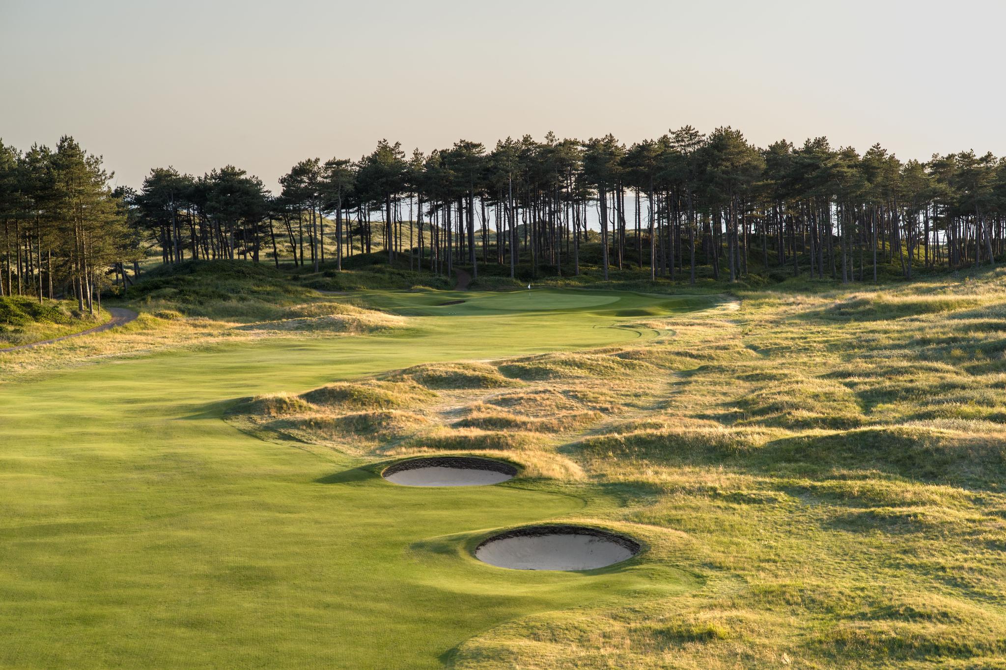 A winding fairway nestled with sand bunkers under clear skies