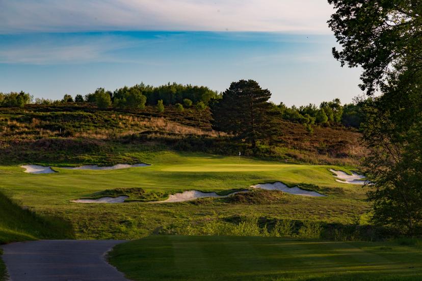 Panoramic view of a winding fairway leading to a smooth elevated green surrounded by sand bunkers