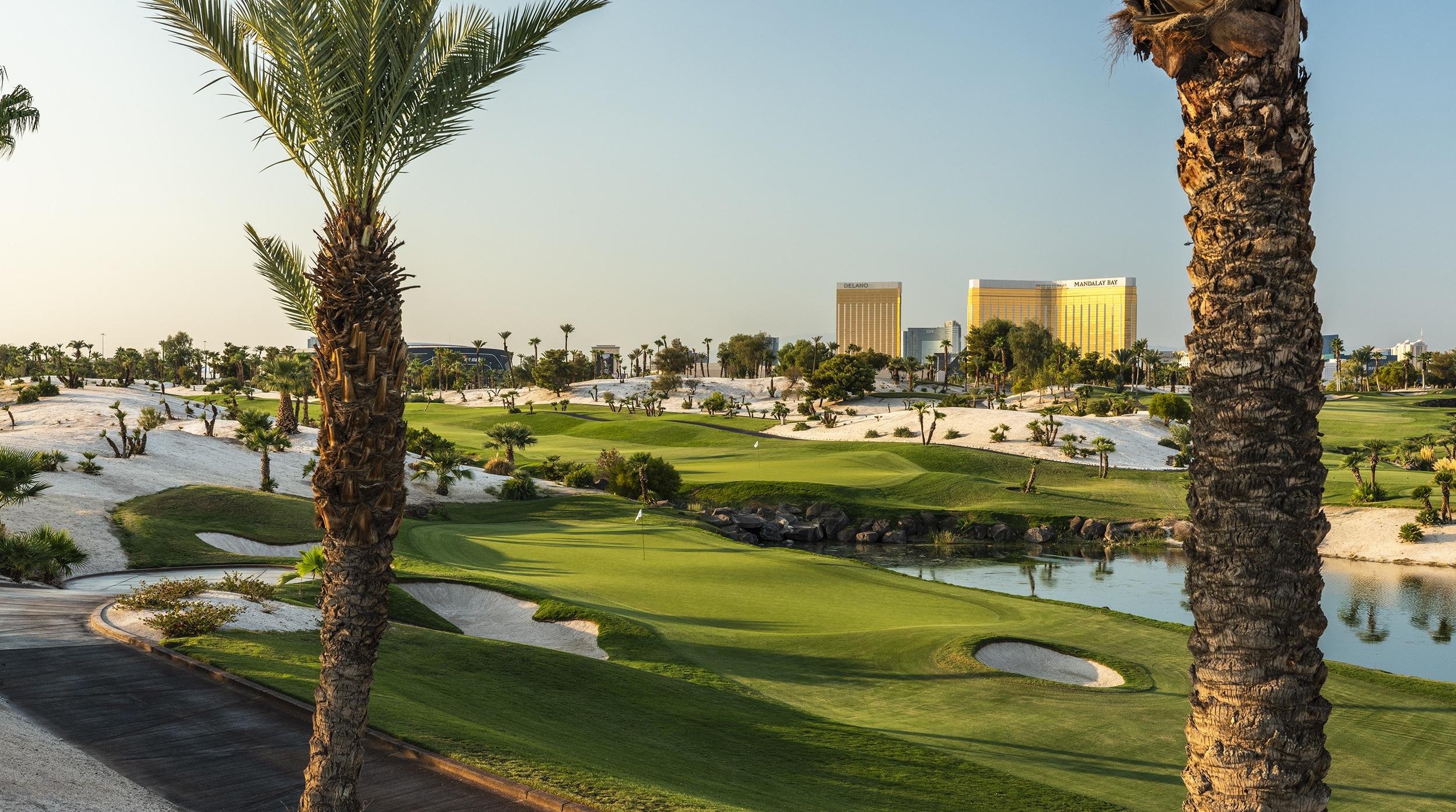 Smooth green at the course surrounded by a water hazard and sand bunkers under clear blue skies