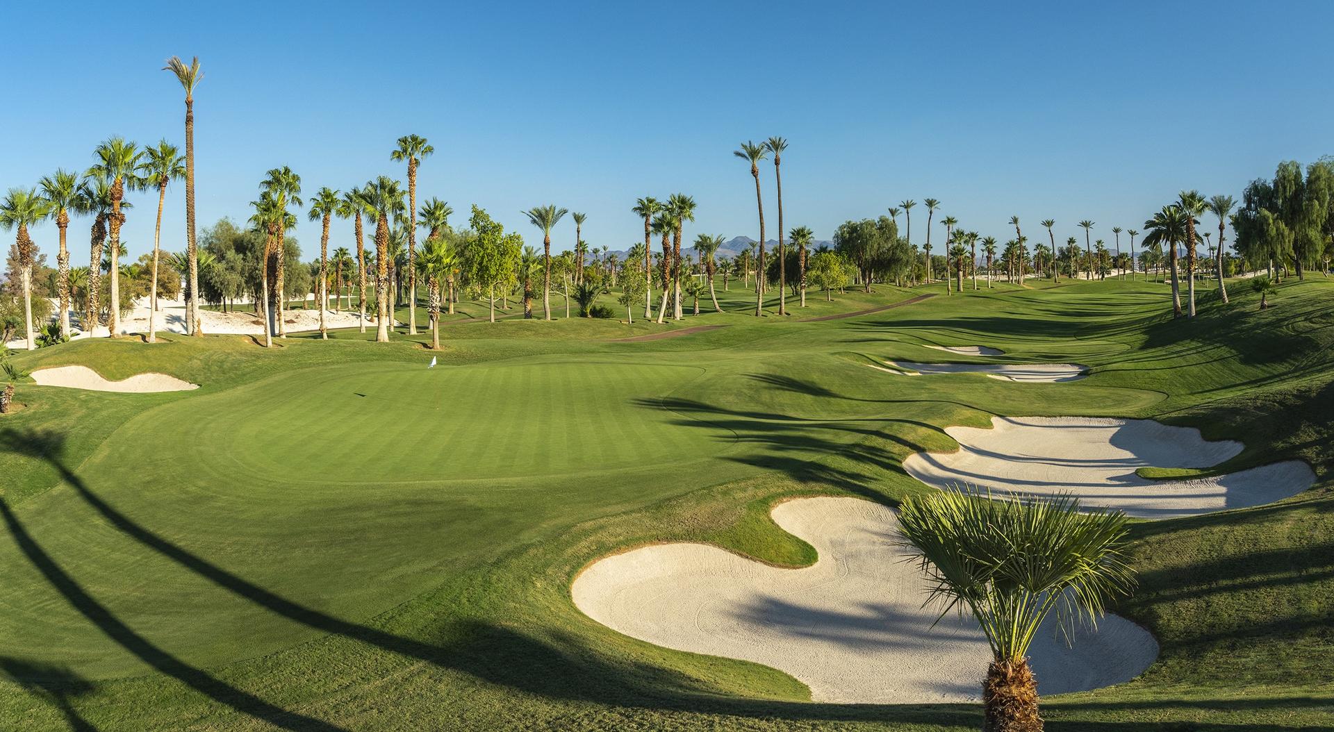 Panoramic angle of a straight fairway leading to a smooth green surrounded by sand bunkers under clear blue skies