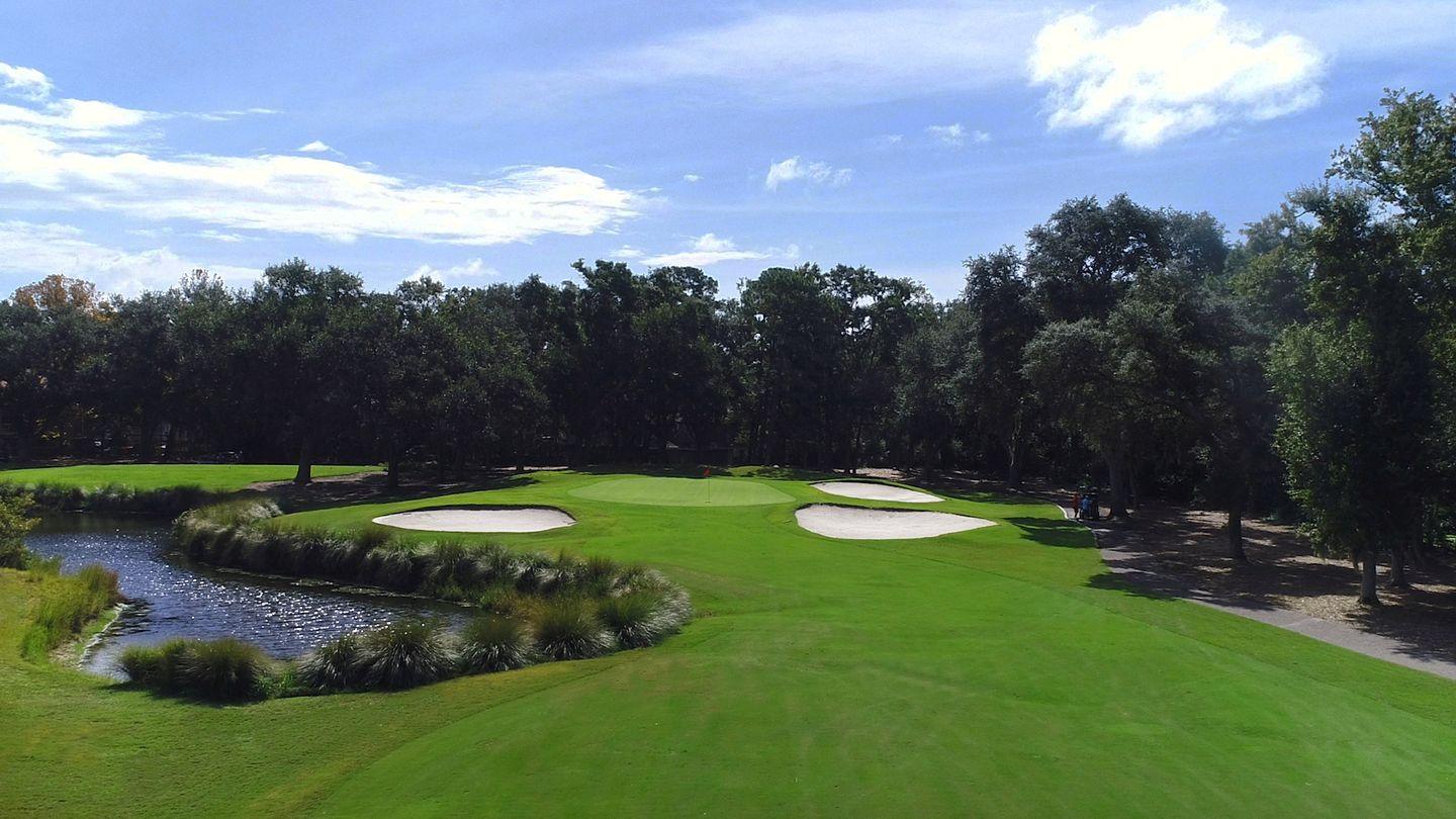 A lush green golf course with bunkers beside a calm water hazard.