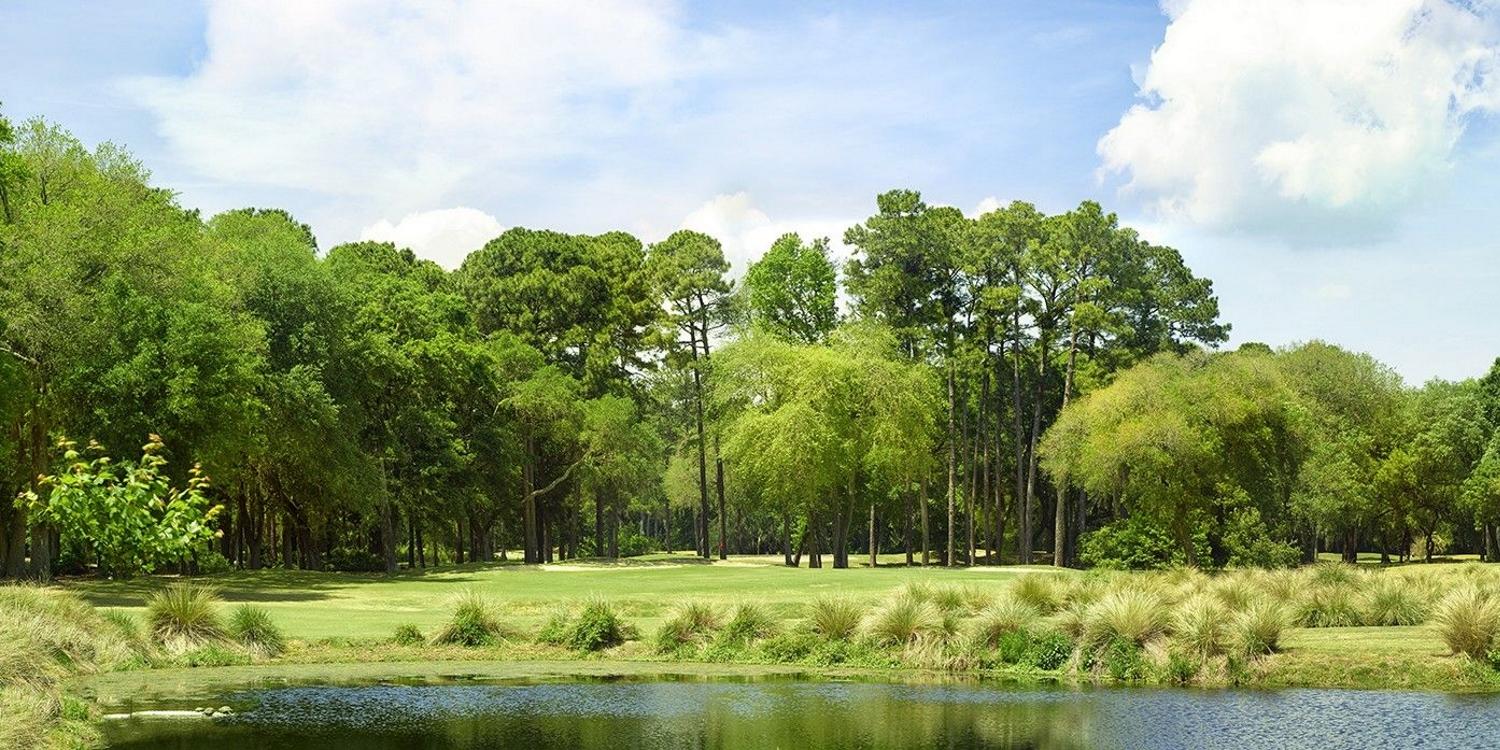 A tranquil green surrounded by trees and a reflective pond.