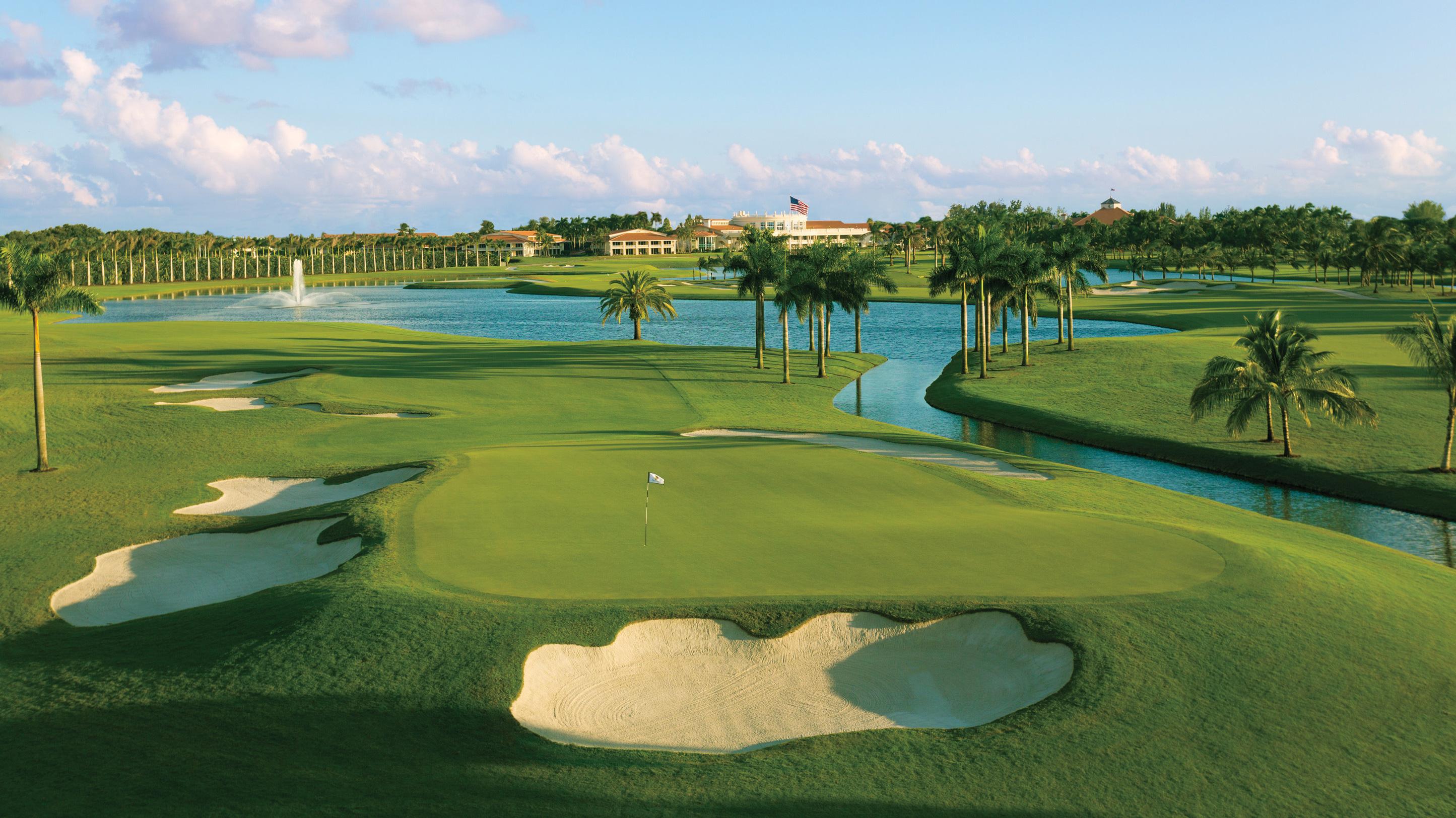 A scenic golf course surrounded by palm trees, with water hazards weaving through the greens and a clubhouse in the distance.