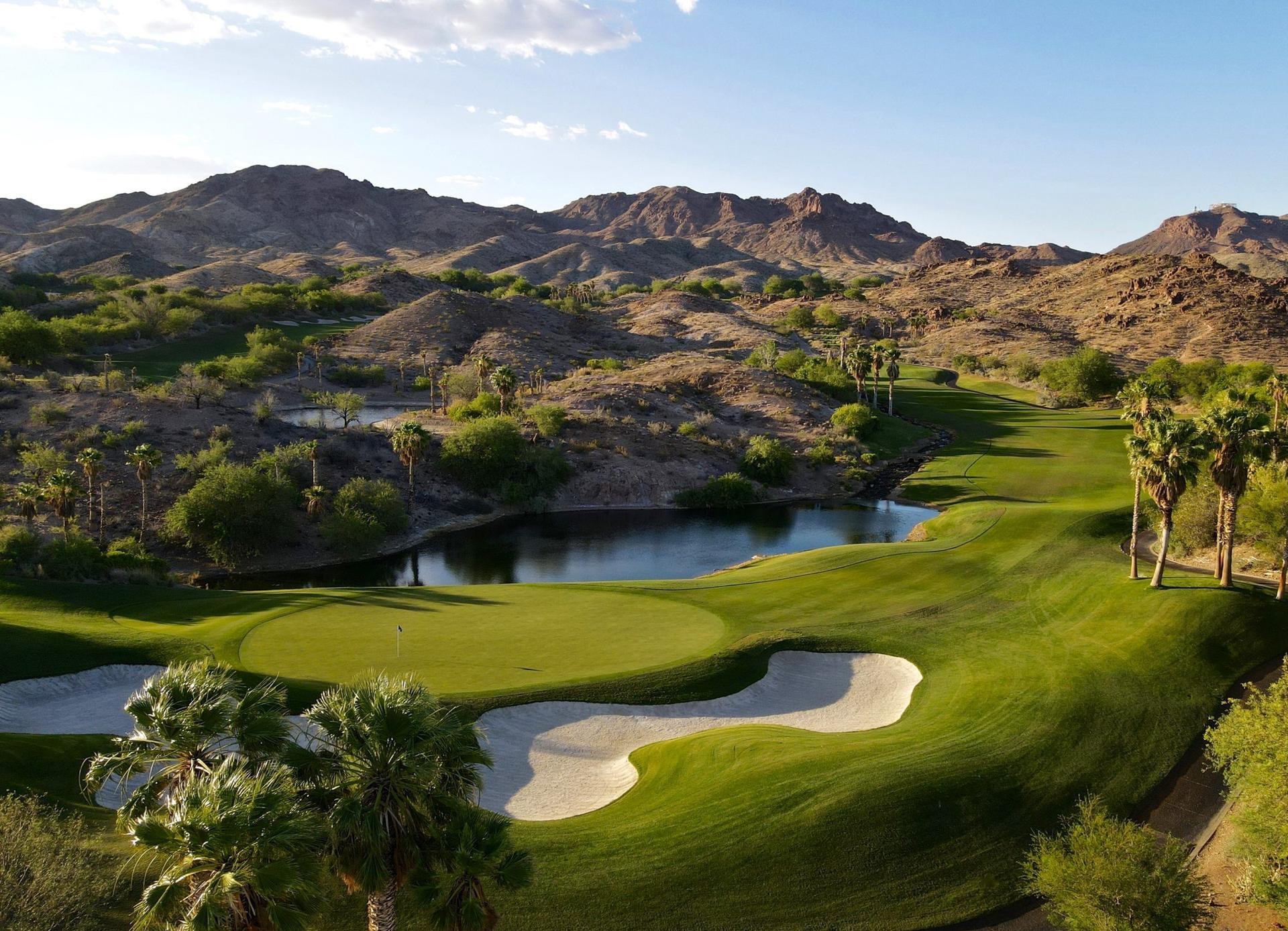 Close-up of a golf green surrounded by sand traps and a tranquil pond.