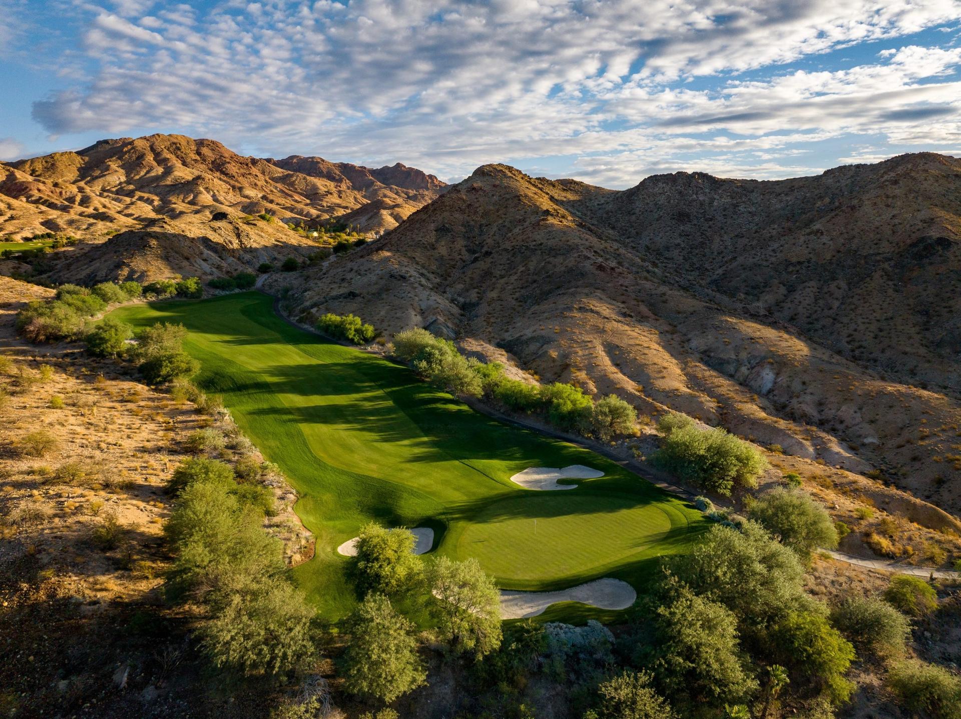 Picturesque golf course hole framed by rocky hills and dramatic skies.