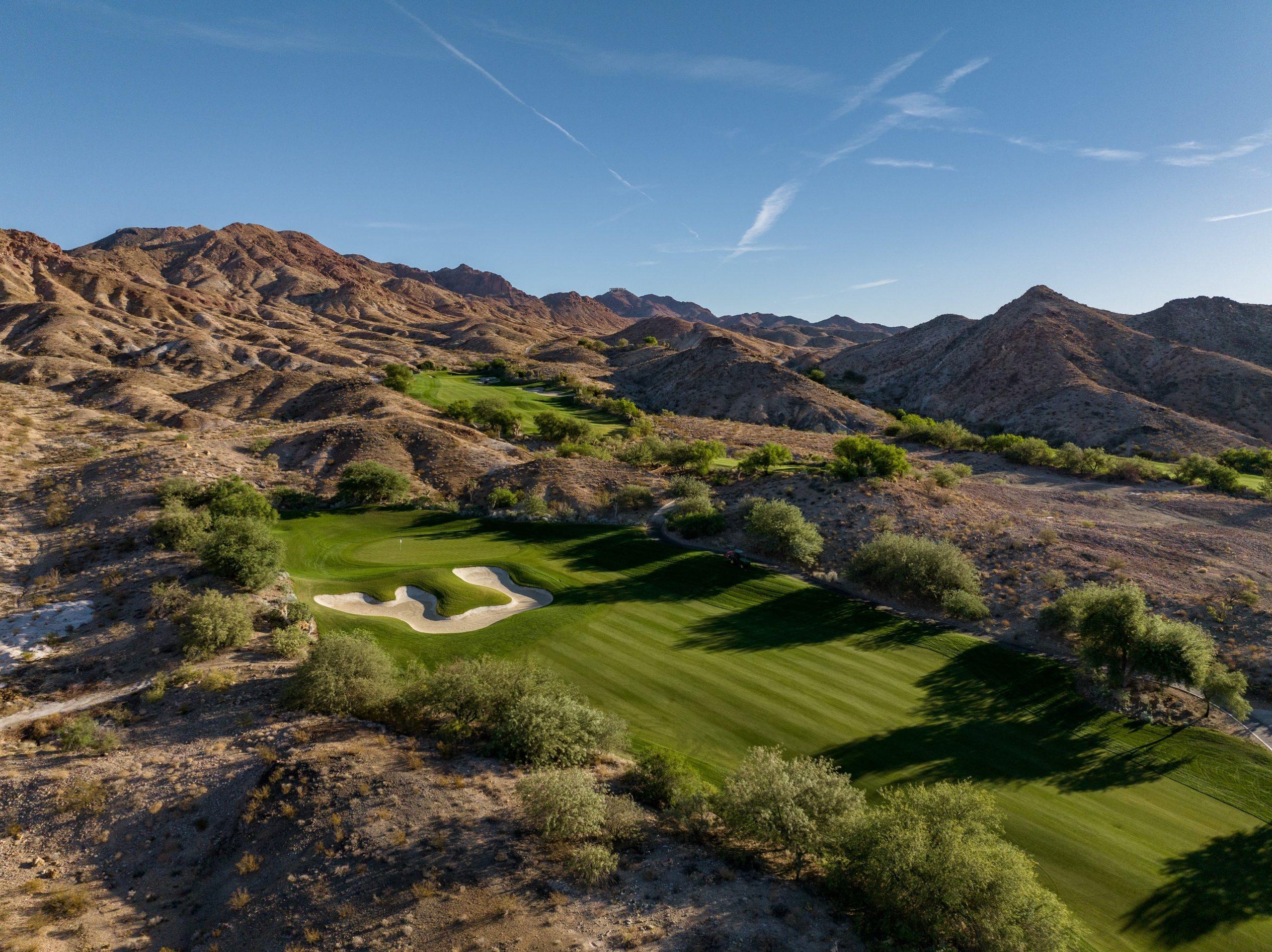 Wide fairway with unique sand bunkers set against a desert mountain backdrop.