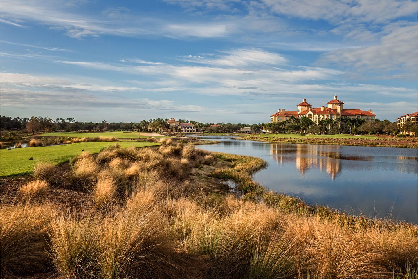 A peaceful waterway lined with golden grasses and resort buildings in the distance.