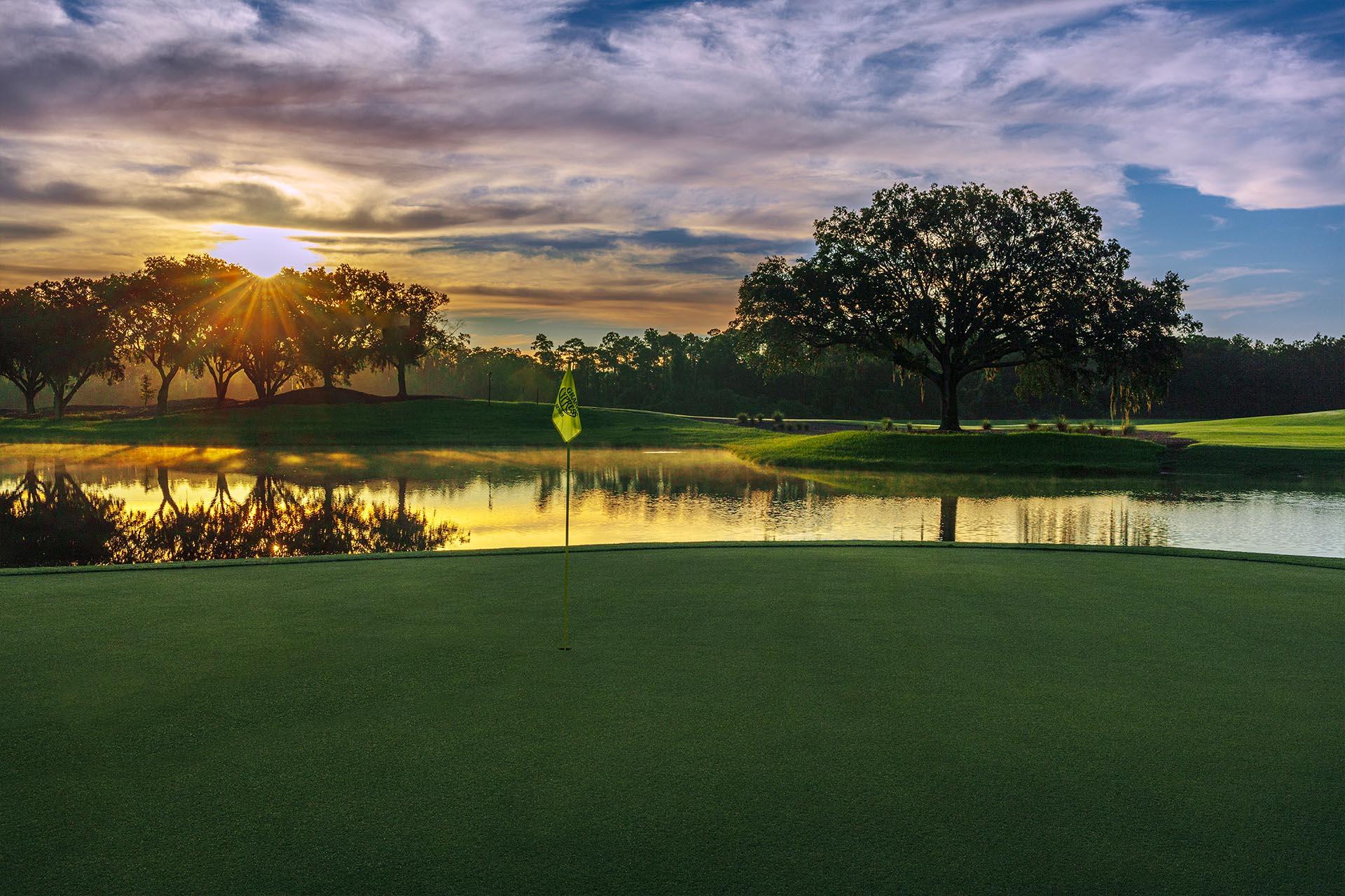 A stunning sunrise over a reflective lake beside the green creates a peaceful and dramatic start to the day.