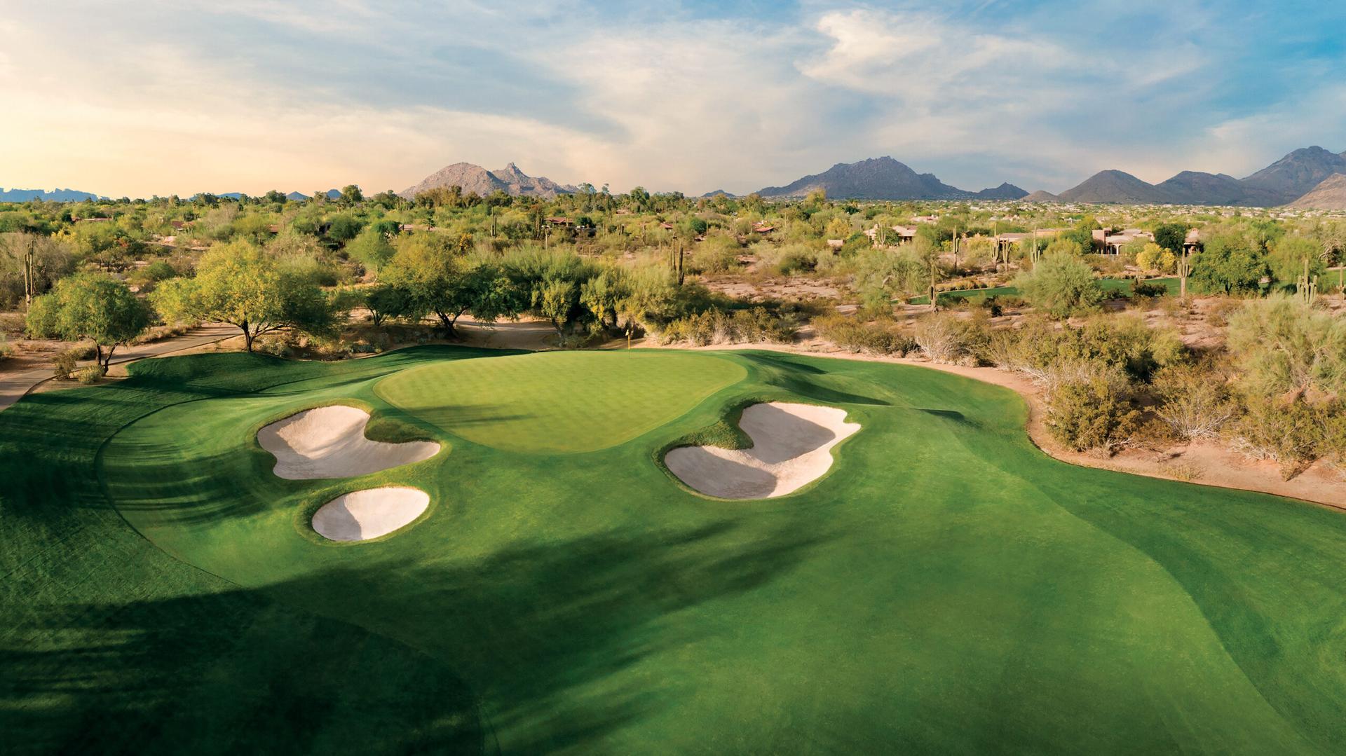 Elevated green surrounded by sand bunkers with mountain views in the distance