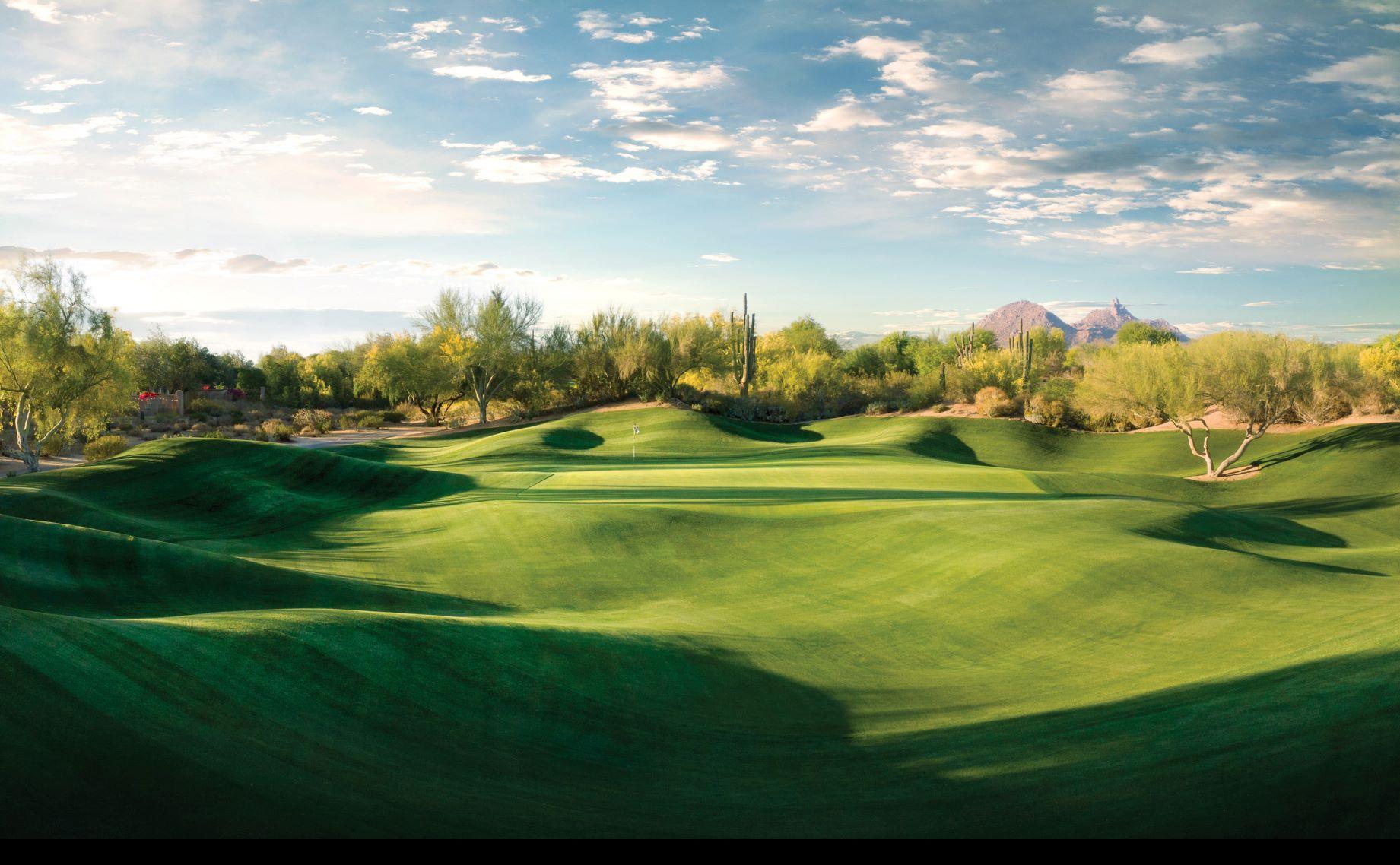 Rolling dunes surrounding a manicured green under blue skies at the Talon Course