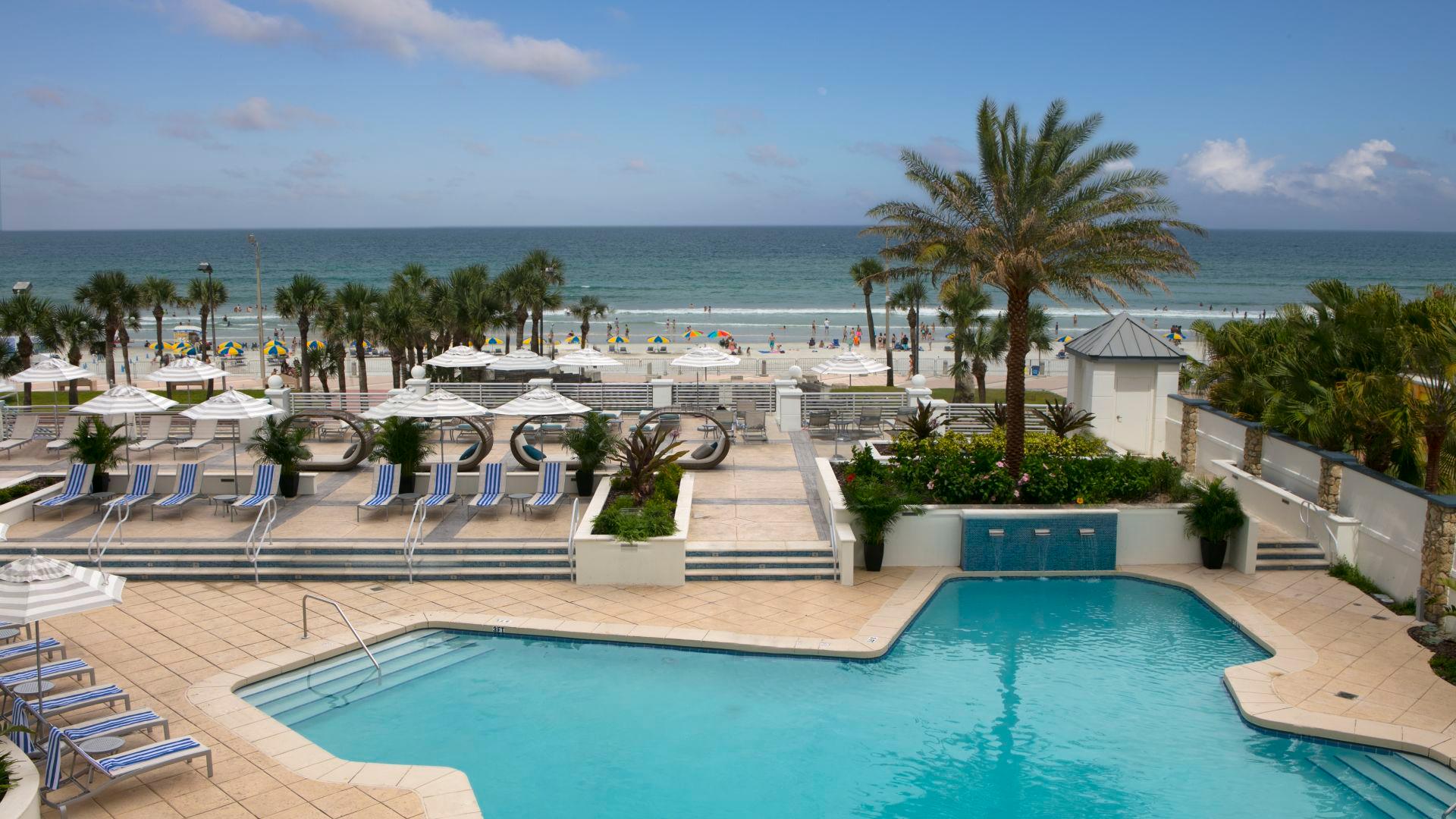 Outdoor swimming pool at the Hilton Daytona with palm trees, sun beds and the option of the beach