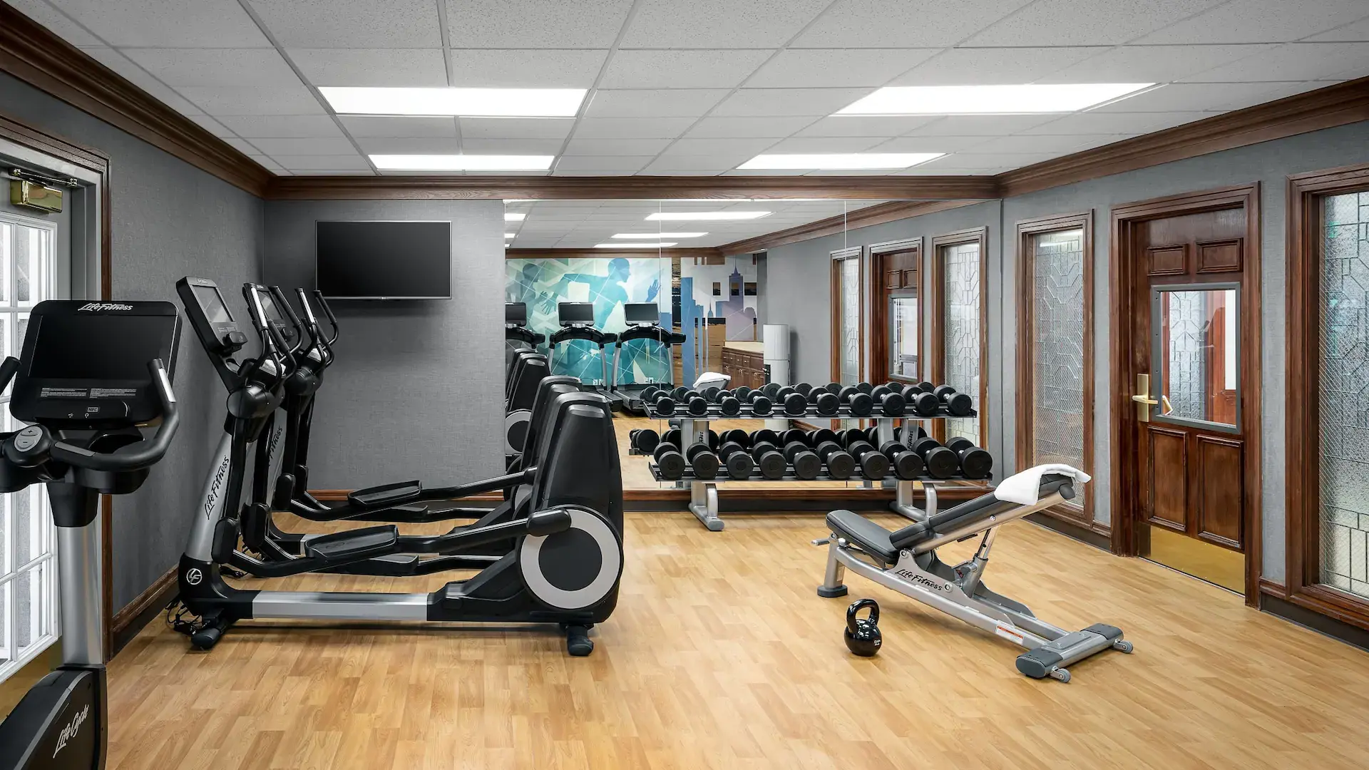 Gym facility at the hotel with multiple cardio machines a weight rack in front of a large window