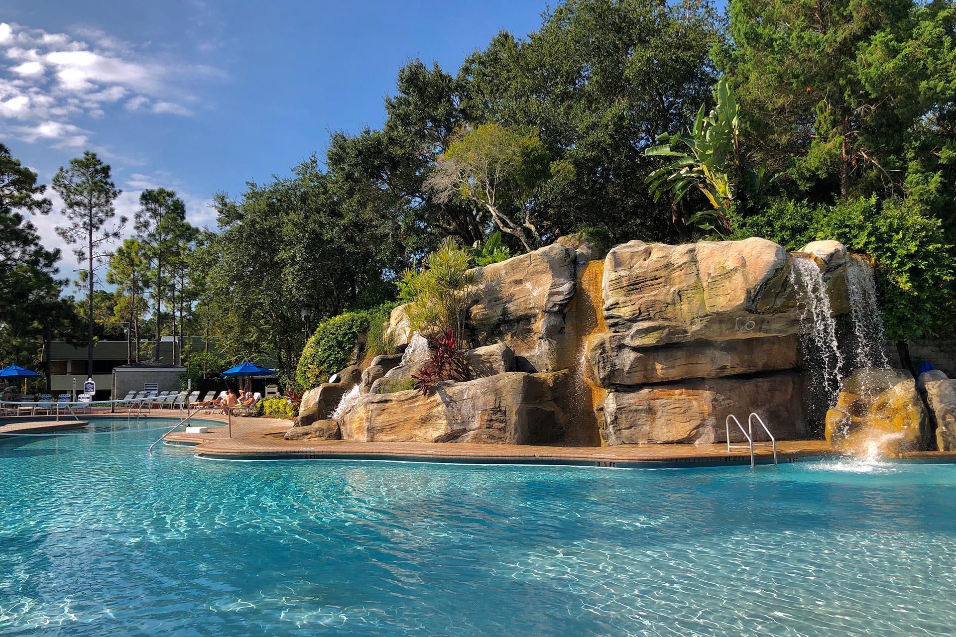 Swimming pool with a rock designed water fountain, sun beds and net set up for water polo