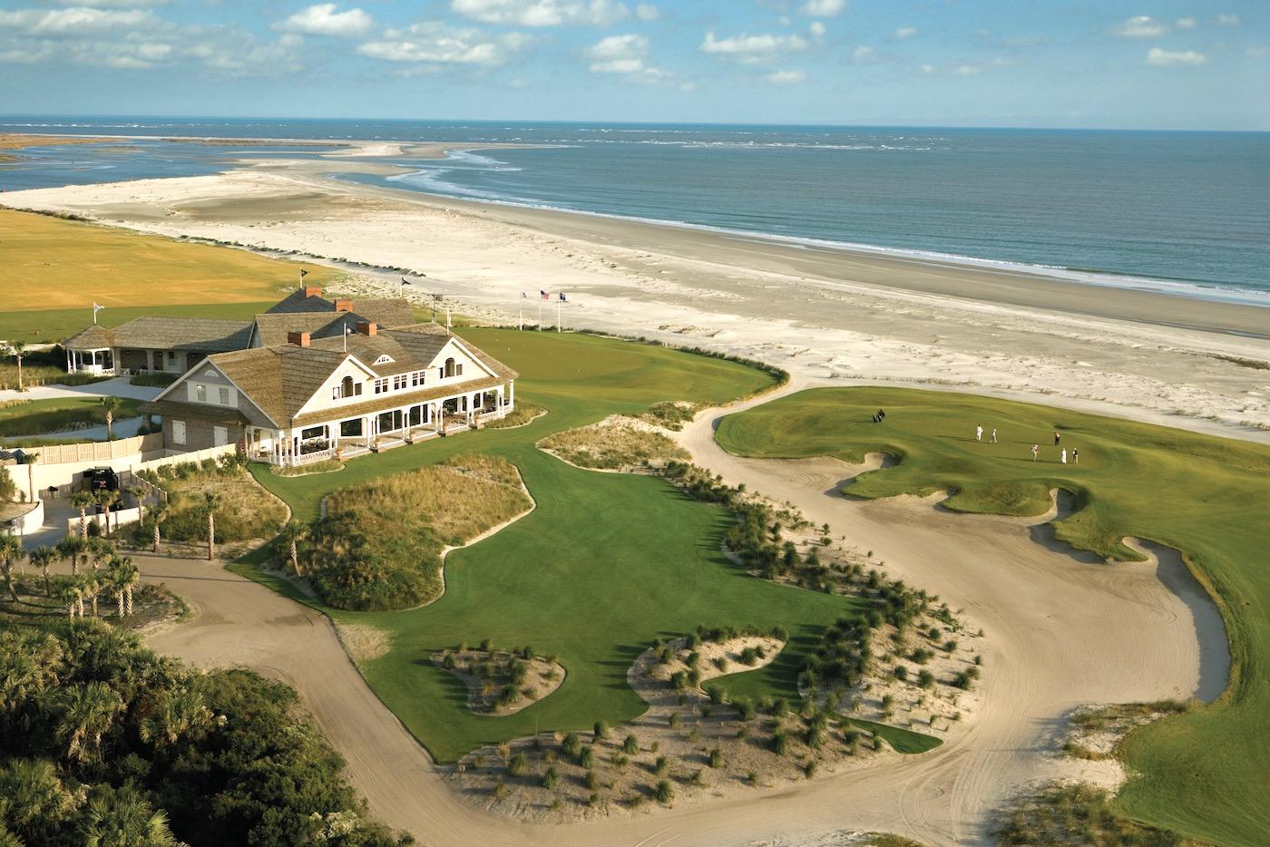 A stunning oceanfront golf course with a clubhouse and sandy dunes beside the beach.