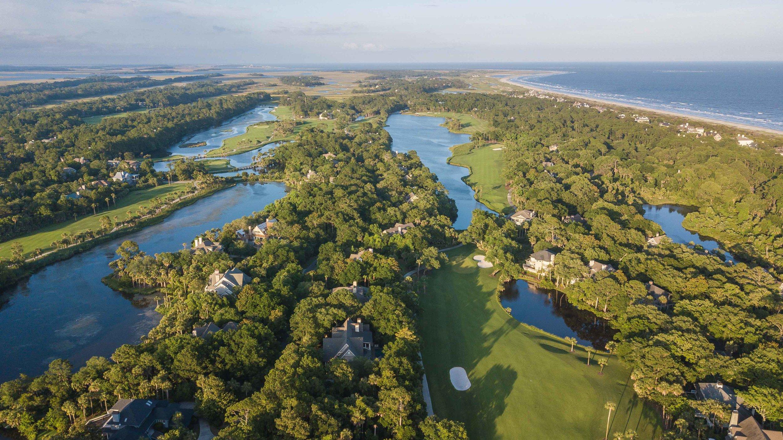 Aerial view of a lush golf course surrounded by waterways and coastline.