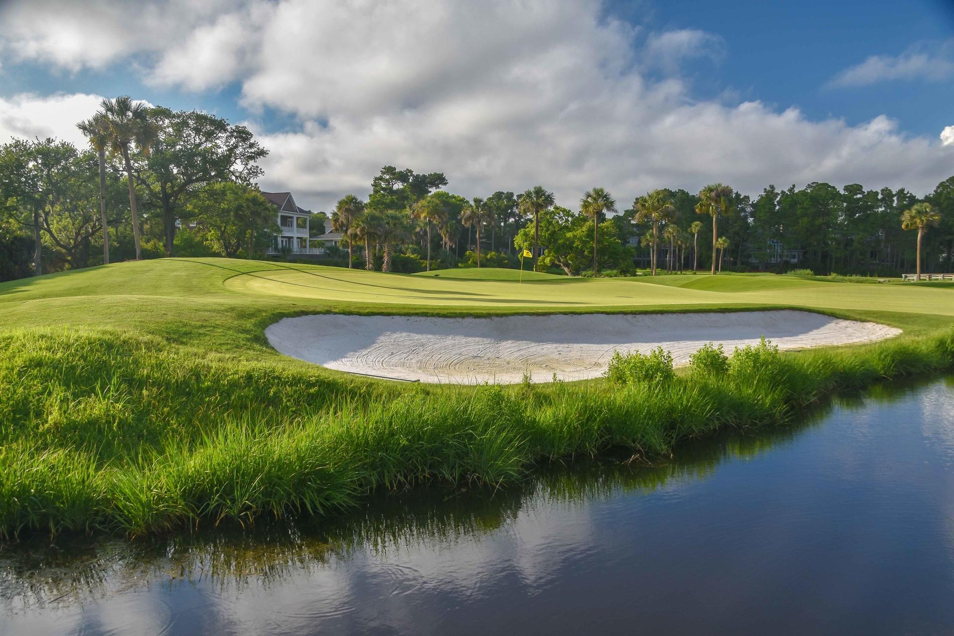Close-up of a green with a sand bunker and water reflecting the sky.