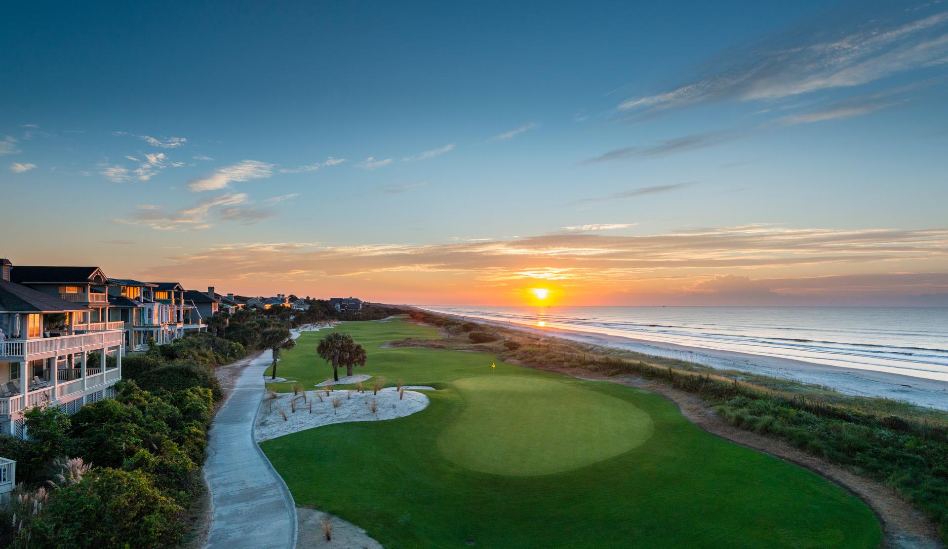 Sun setting over a straight fairway leading to a smooth green with coastal views