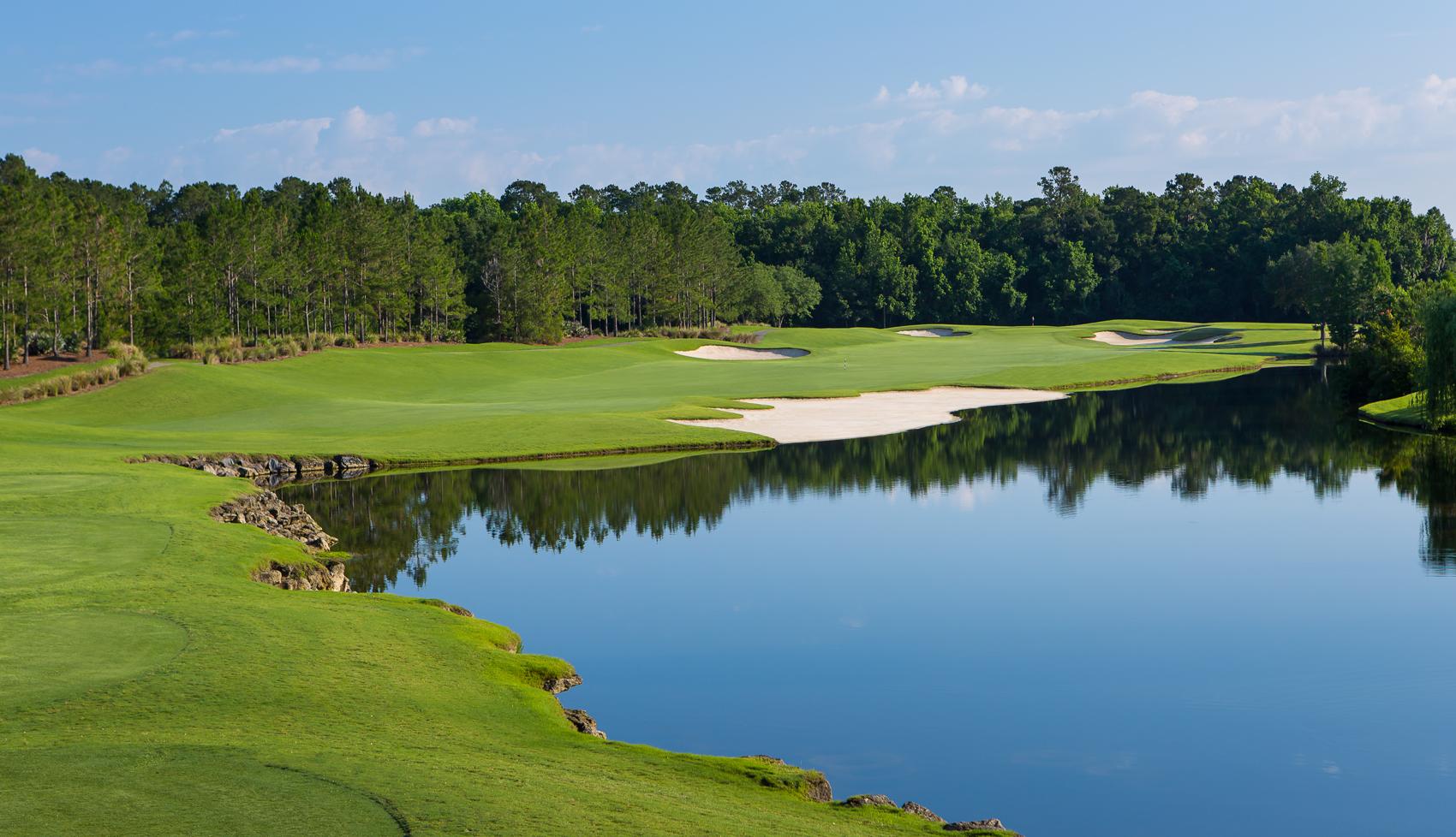 Large pond neighbouring uniquely shaped sand bunkers littered around the green