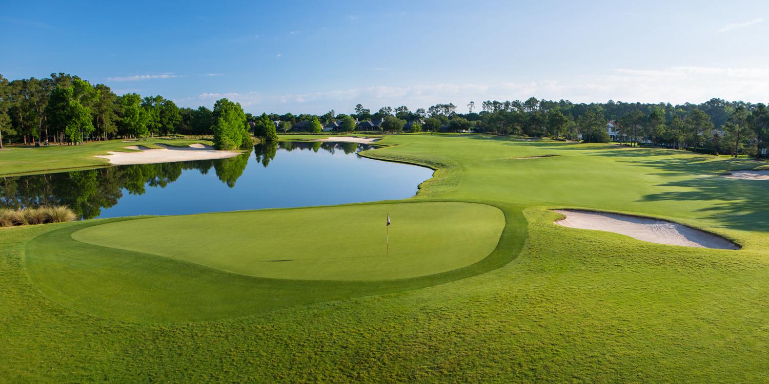 Panoramic view of a wide fairway leading to a well maintained green next to a large pond