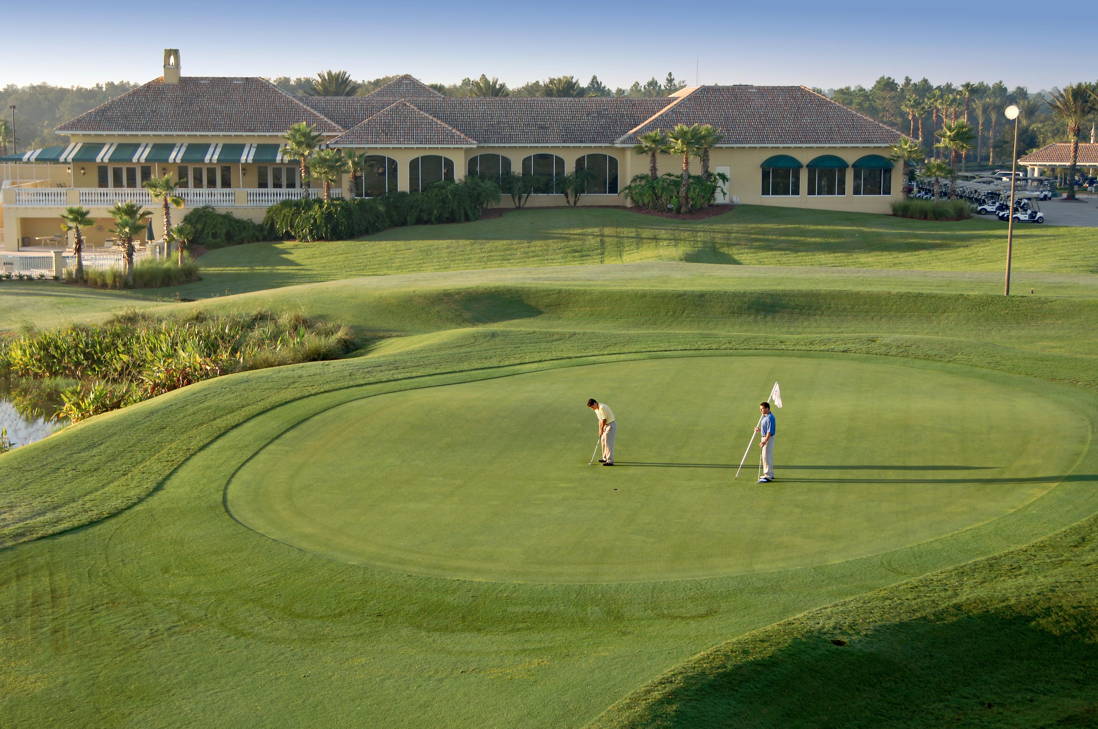 Two golfers play near the green at LPGA International Hills, with the clubhouse in the background.