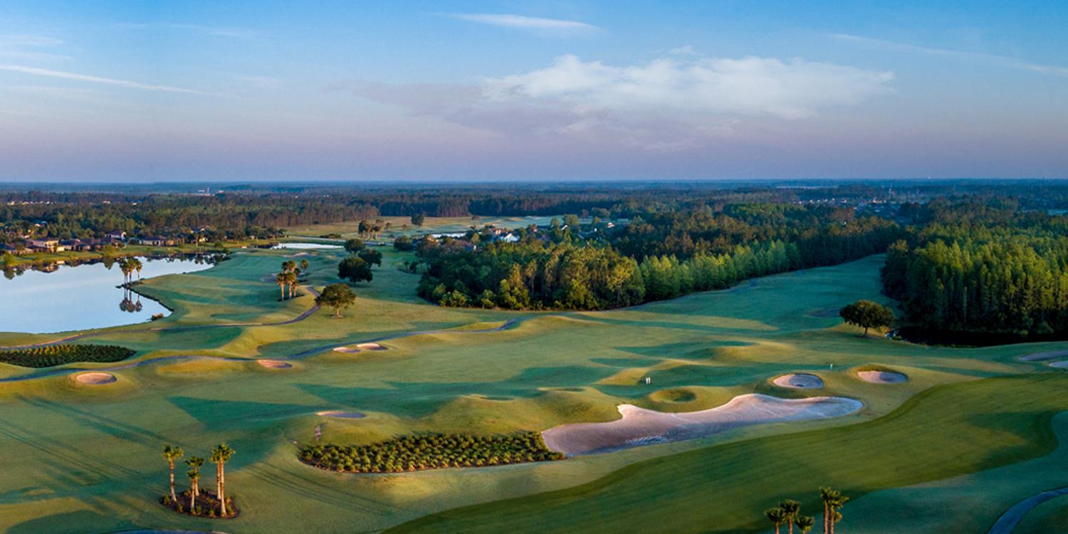 A sweeping view of the golf course surrounded by water and trees under a serene sky.