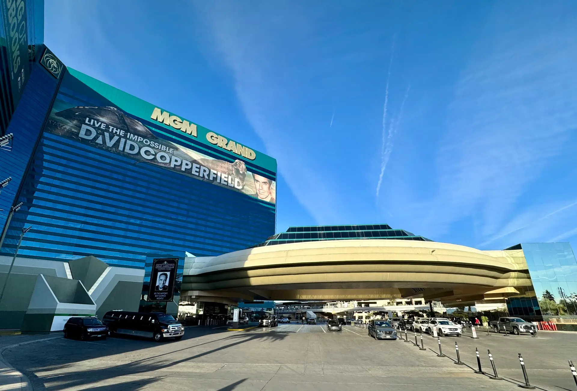 Front entrance to the resort featuring cars in the pick up/ drop off section with the building towering over