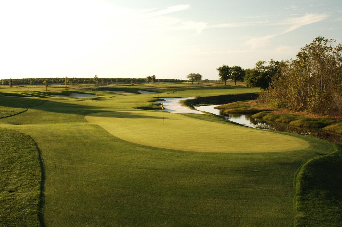 Sun setting over a smooth green placed next to a sand bunker and water feature at the National Course