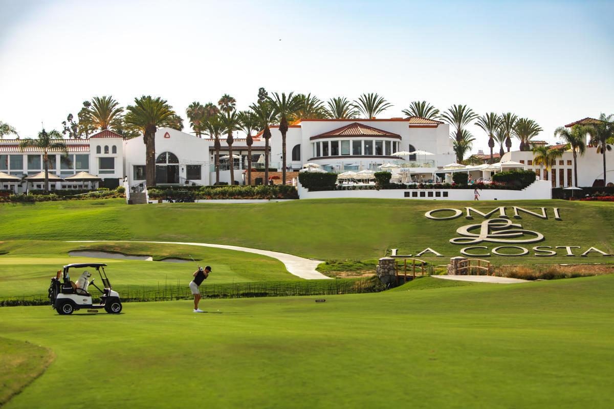 Golfer hitting towards the green next to the company logo nestled into the grass with the resort building over looking