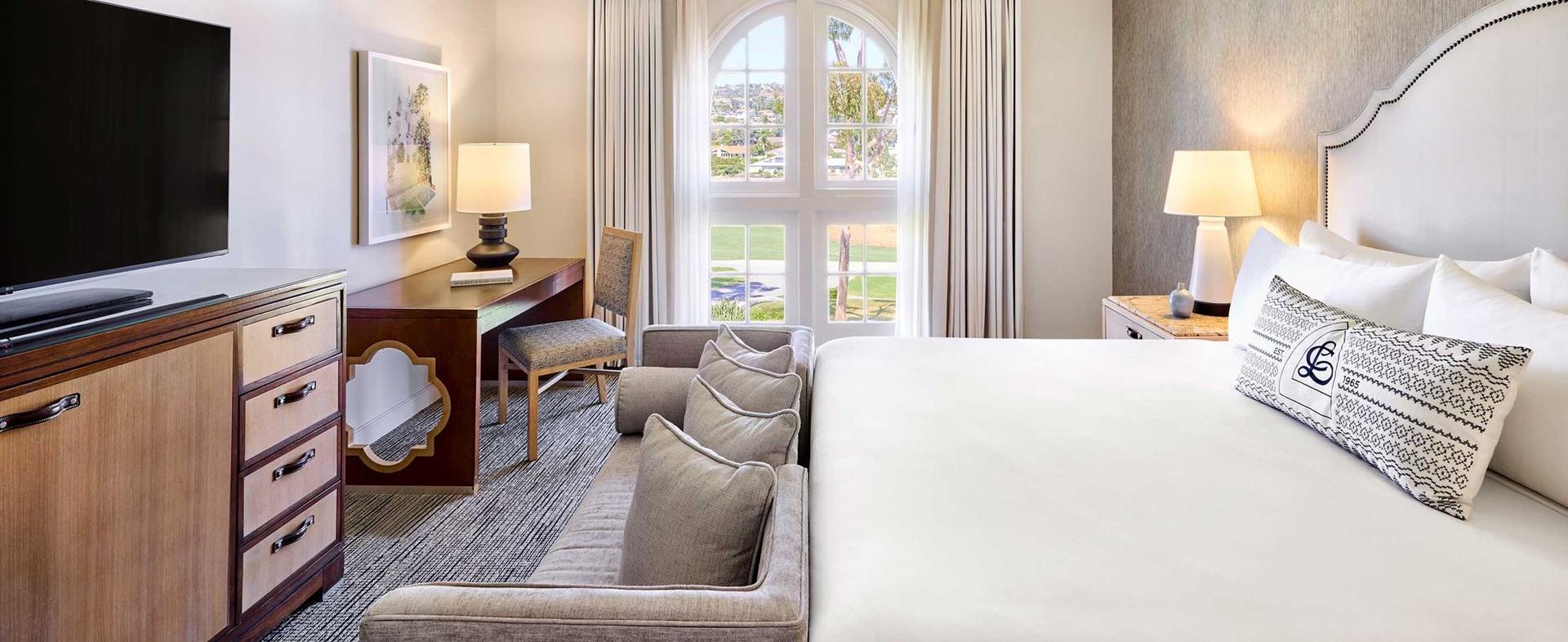 Modern double bed room at the resort with a sofa sandwiched between the bed and TV alongside window views of the course