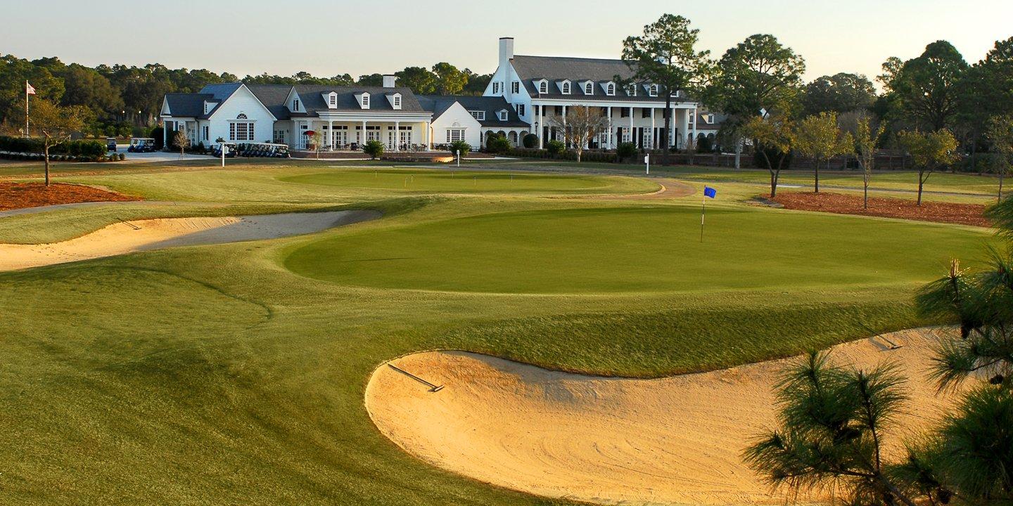The clubhouse looking out onto a smooth green next to a sand bunker
