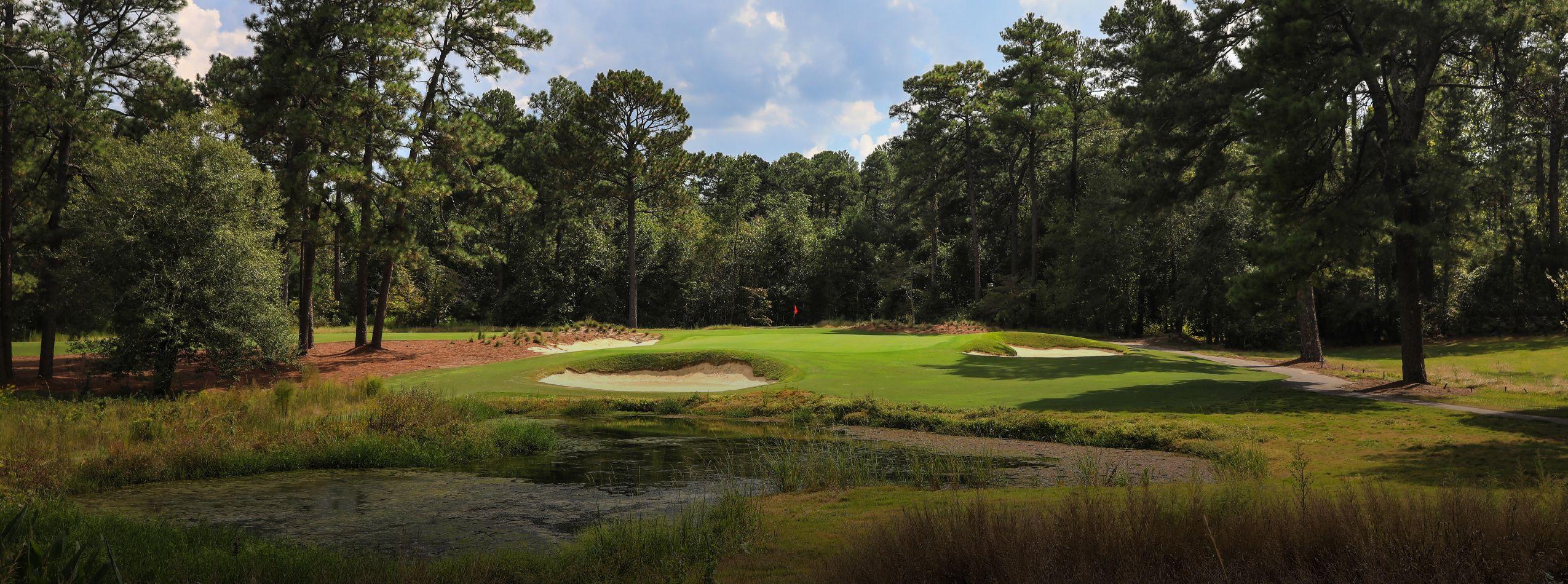 Serene golf hole with water hazard surrounded by towering pines and lush vegetation.