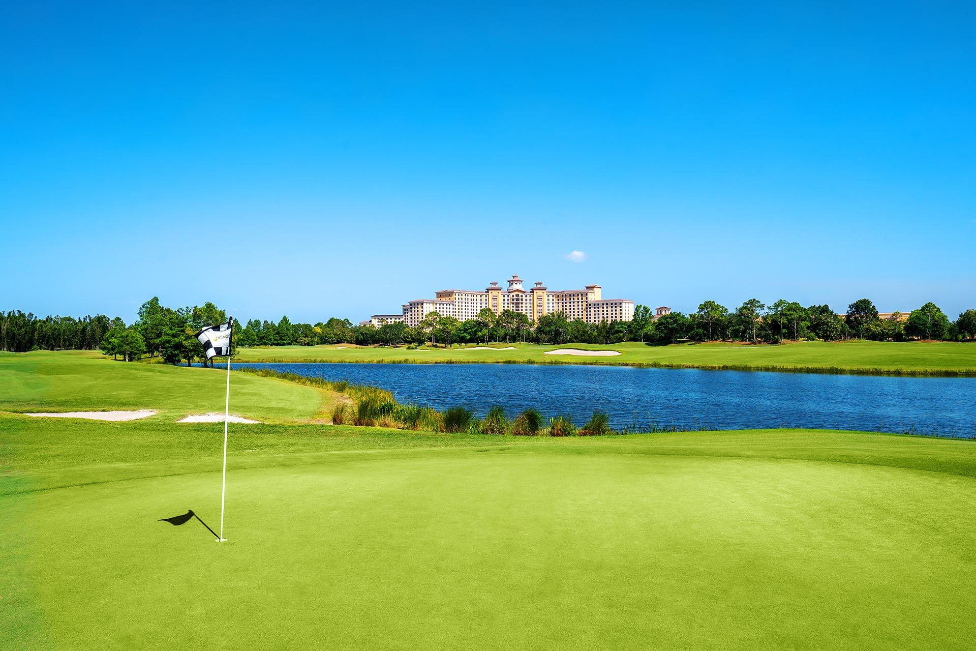 A flagstick near the water with a grand resort rising in the distance.