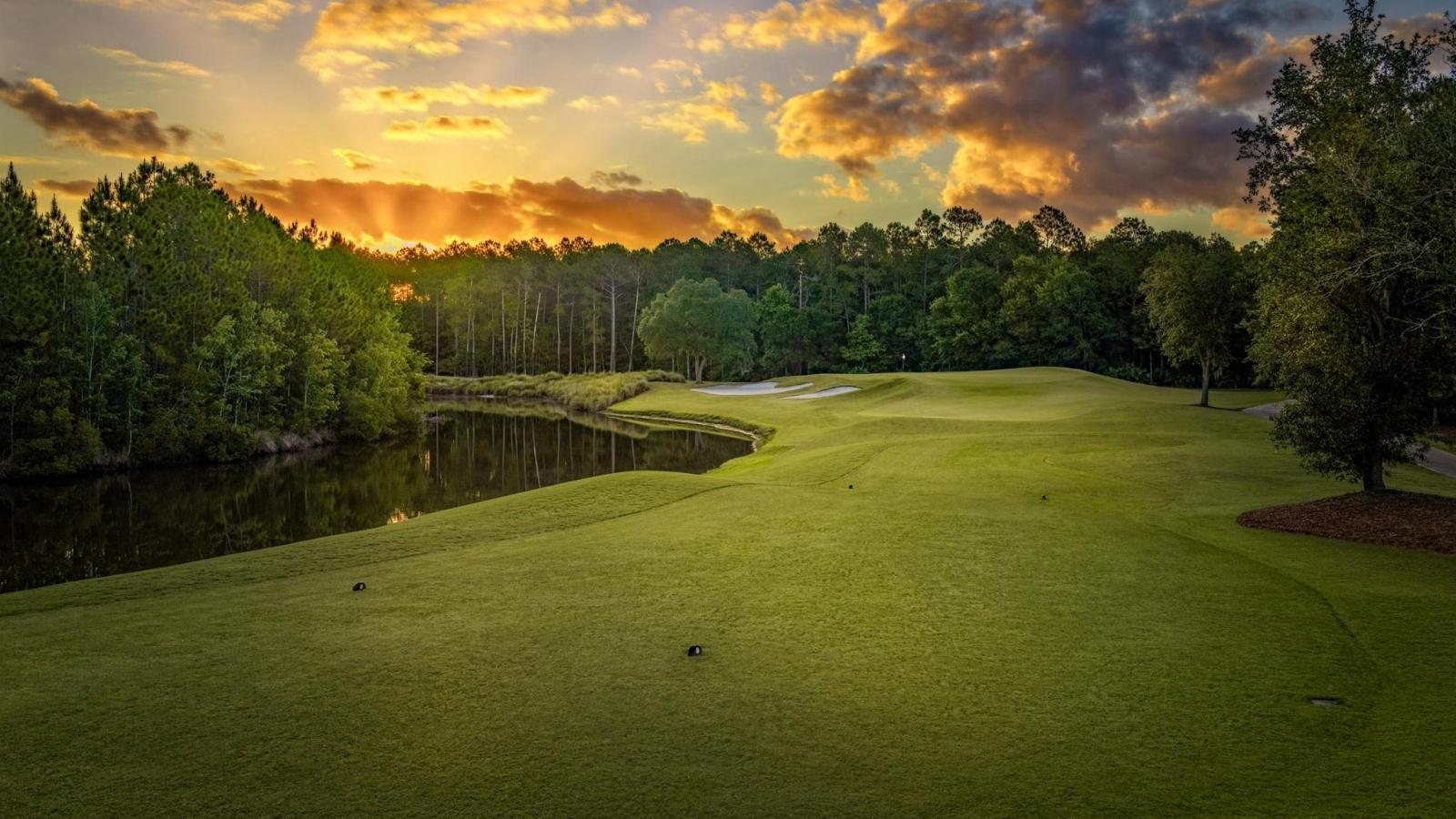 The sun sets over a serene green, casting a golden glow across the course and surrounding forest.