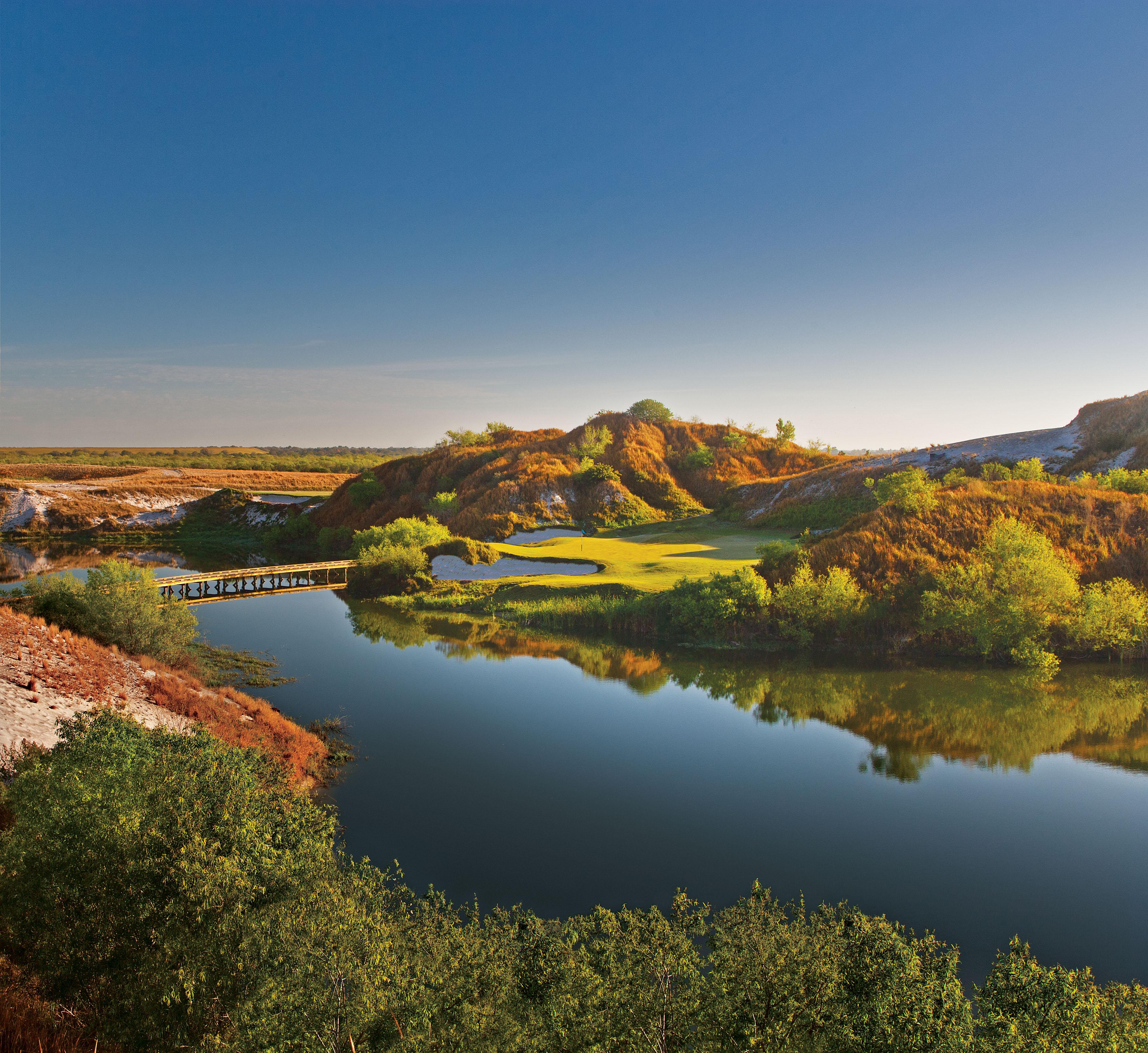 Smooth green placed between mountains with a bridge over the lake to navigate the course
