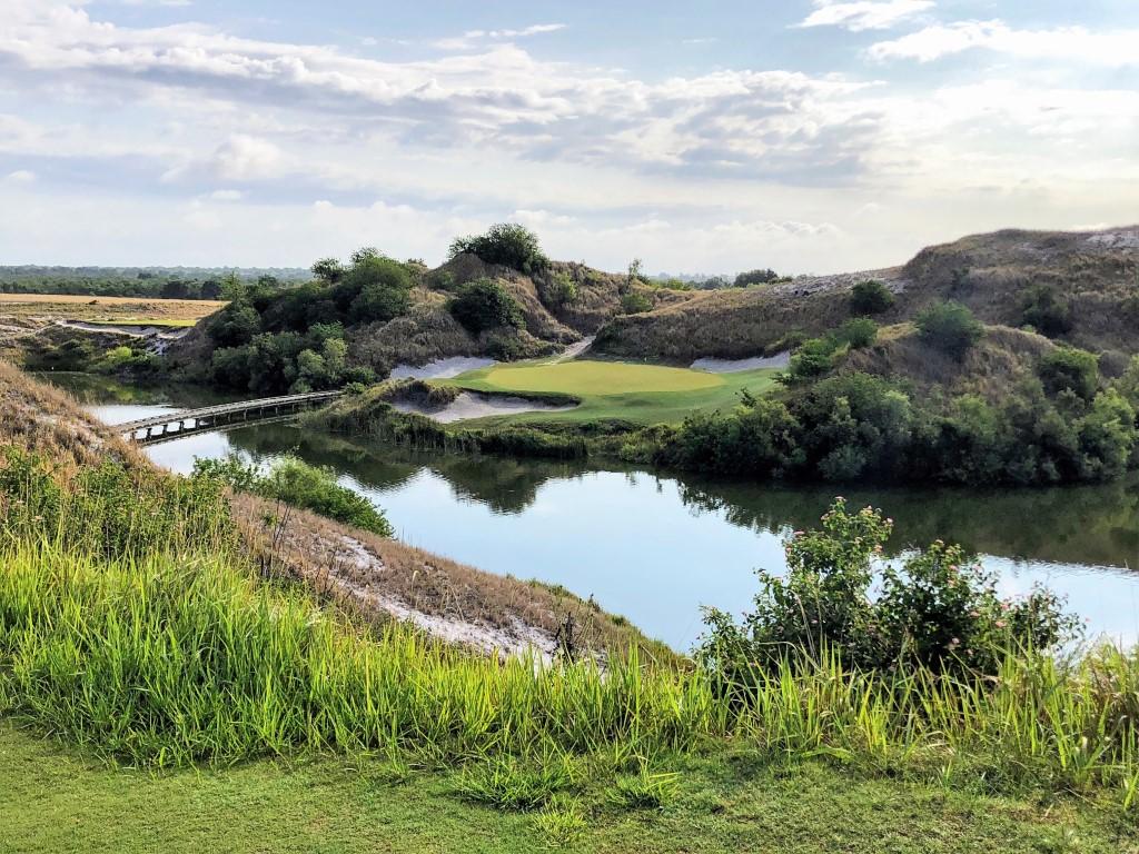 Elevated green accessed by a wooden bridge over water.