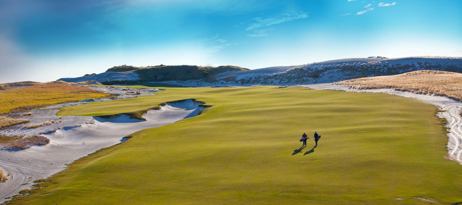 Two golfers enjoying their round the wide fairway under clear blue skies