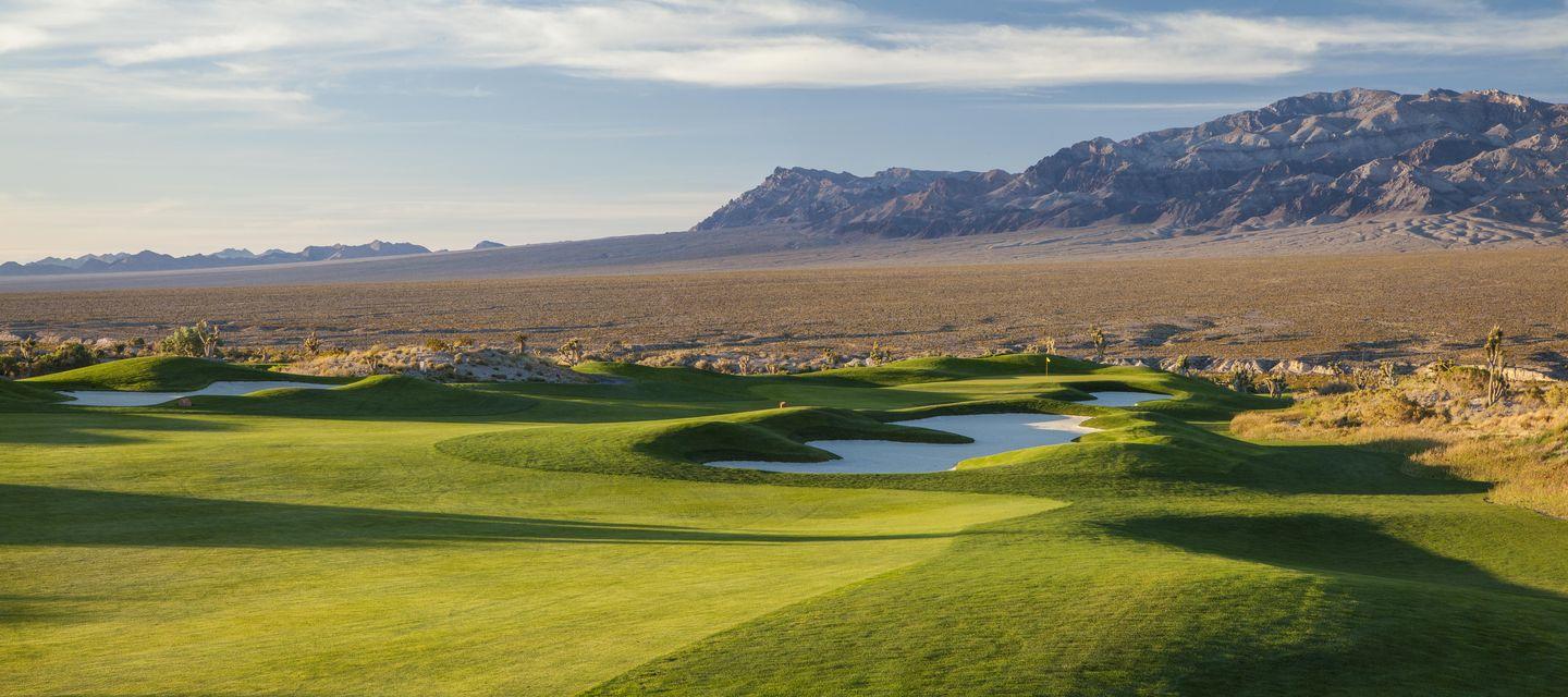 Panoramic view of A large sand bunker next to a smooth green with mountains views in the back