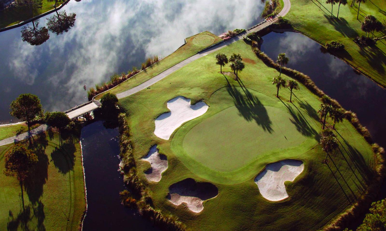 Aerial view of an island like green surrounded by bunkers and a water hazard that runs through the course.