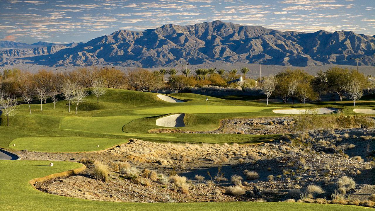 Panoramic view of mountains towing over a well maintained green surrounded by bunkers on the TPC Las Vegas course