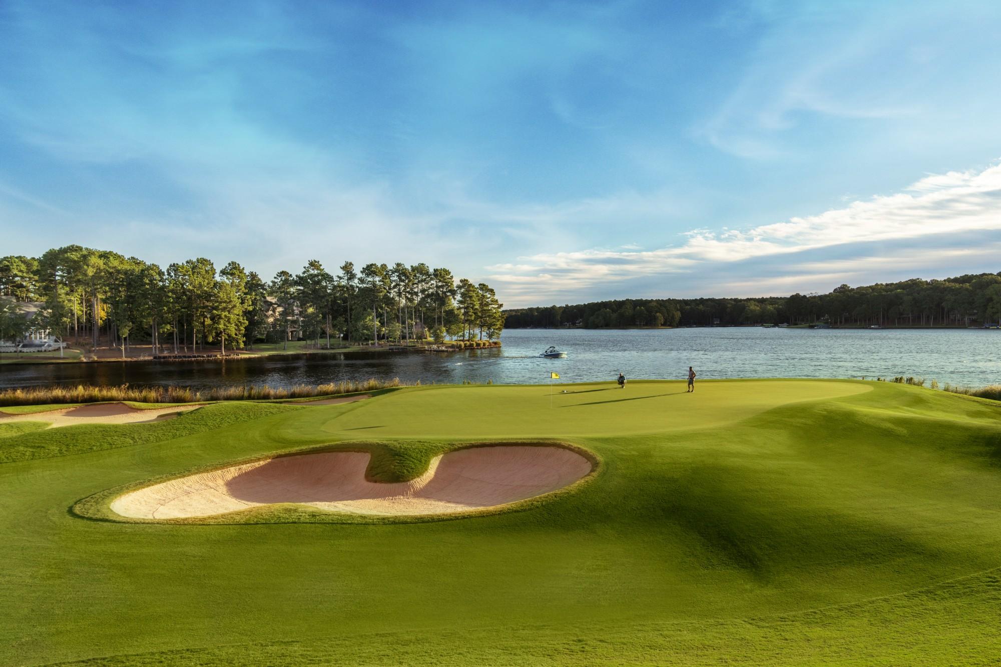 Golfers enjoying their round on an elevated green with a large sand bunker and lake views